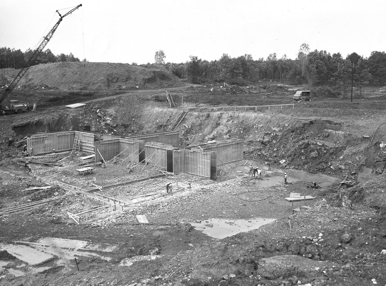 At its founding, the Marshall Space Flight Center (MSFC) inherited the Army’s Jupiter and Redstone test stands, but much larger facilities were needed for the giant stages of the Saturn V. From 1960 to 1964, the existing stands were remodeled and a sizable new test area was developed. The new comprehensive test complex for propulsion and structural dynamics was unique within the nation and the free world, and they remain so today because they were constructed with foresight to meet the future as well as on going needs. Construction of the S-IC Static test stand complex began in 1961 in the west test area of MSFC, and was completed in 1964. The S-IC static test stand was designed to develop and test the 138-ft long and 33-ft diameter Saturn V S-IC first stage, or booster stage, weighing in at 280,000 pounds. Required to hold down the brute force of a 7,500,000-pound thrust produced by 5 F-1 engines, the S-IC static test stand was designed and constructed with the strength of hundreds of tons of steel and 12,000,000 pounds of cement, planted down to bedrock 40 feet below ground level. The foundation walls, constructed with concrete and steel, are 4 feet thick. The base structure consists of four towers with 40-foot-thick walls extending upward 144 feet above ground level. The structure was topped by a crane with a 135-foot boom. With the boom in the upright position, the stand was given an overall height of 405 feet, placing it among the highest structures in Alabama at the time. This photo shows the construction progress of the forms for the concrete foundation walls as of September 7, 1961.