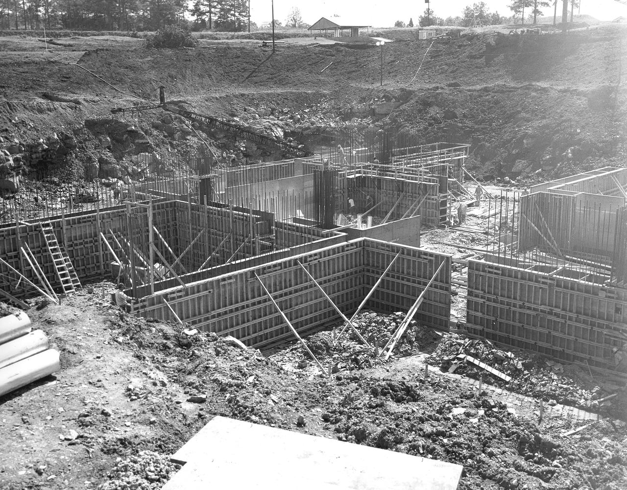 At its founding, the Marshall Space Flight Center (MSFC) inherited the Army’s Jupiter and Redstone test stands, but much larger facilities were needed for the giant stages of the Saturn V. From 1960 to 1964, the existing stands were remodeled and a sizable new test area was developed. The new comprehensive test complex for propulsion and structural dynamics was unique within the nation and the free world, and they remain so today because they were constructed with foresight to meet the future as well as on going needs. Construction of the S-IC Static test stand complex began in 1961 in the west test area of MSFC, and was completed in 1964. The S-IC static test stand was designed to develop and test the 138-ft long and 33-ft diameter Saturn V S-IC first stage, or booster stage, weighing in at 280,000 pounds. Required to hold down the brute force of a 7,500,000-pound thrust produced by 5 F-1 engines, the S-IC static test stand was designed and constructed with the strength of hundreds of tons of steel and 12,000,000 pounds of cement, planted down to bedrock 40 feet below ground level. The foundation walls, constructed with concrete and steel, are 4 feet thick. The base structure consists of four towers with 40-foot-thick walls extending upward 144 feet above ground level. The structure was topped by a crane with a 135-foot boom. With the boom in the upright position, the stand was given an overall height of 405 feet, placing it among the highest structures in Alabama at the time. This photo, taken September 15, 1961, shows the installation of the reinforcing steel prior to the pouring of the concrete foundation walls.