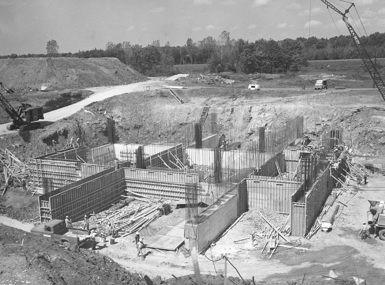 At its founding, the Marshall Space Flight Center (MSFC) inherited the Army’s Jupiter and Redstone test stands, but much larger facilities were needed for the giant stages of the Saturn V. From 1960 to 1964, the existing stands were remodeled and a sizable new test area was developed. The new comprehensive test complex for propulsion and structural dynamics was unique within the nation and the free world, and they remain so today because they were constructed with foresight to meet the future as well as on going needs. Construction of the S-IC Static test stand complex began in 1961 in the west test area of MSFC, and was completed in 1964. The S-IC static test stand was designed to develop and test the 138-ft long and 33-ft diameter Saturn V S-IC first stage, or booster stage, weighing in at 280,000 pounds. Required to hold down the brute force of a 7,500,000-pound thrust produced by 5 F-1 engines, the S-IC static test stand was designed and constructed with the strength of hundreds of tons of steel and 12,000,000 pounds of cement, planted down to bedrock 40 feet below ground level. The foundation walls, constructed with concrete and steel, are 4 feet thick. The base structure consists of four towers with 40-foot-thick walls extending upward 144 feet above ground level. The structure was topped by a crane with a 135-foot boom. With the boom in the upright position, the stand was given an overall height of 405 feet, placing it among the highest structures in Alabama at the time. This photo, taken September 22, 1961, shows the progress of the concrete walls for the stand’s foundation. Some of the walls have been poured and some of the concrete forms have been removed.