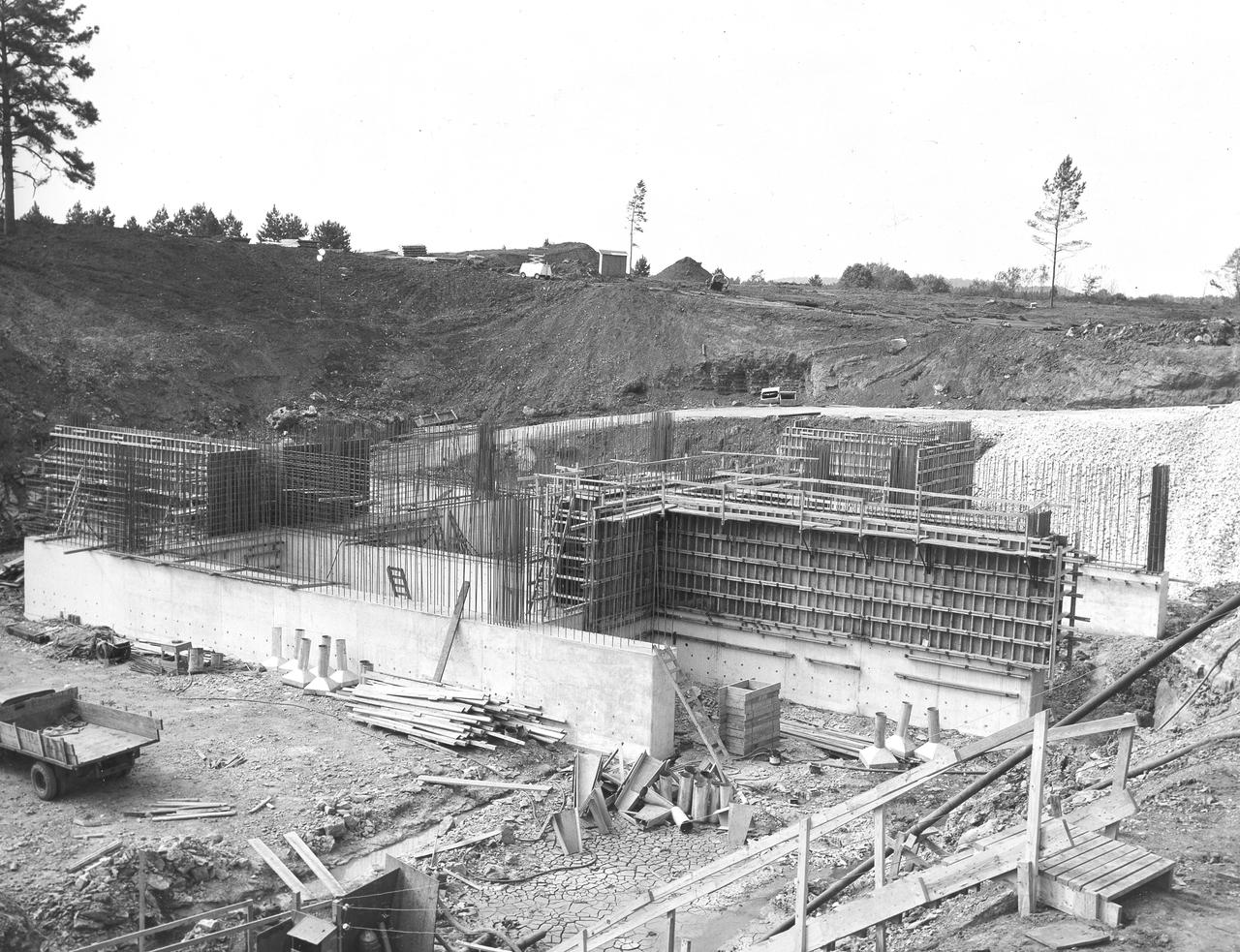 At its founding, the Marshall Space Flight Center (MSFC) inherited the Army’s Jupiter and Redstone test stands, but much larger facilities were needed for the giant stages of the Saturn V. From 1960 to 1964, the existing stands were remodeled and a sizable new test area was developed. The new comprehensive test complex for propulsion and structural dynamics was unique within the nation and the free world, and they remain so today because they were constructed with foresight to meet the future as well as on going needs. Construction of the S-IC Static test stand complex began in 1961 in the west test area of MSFC, and was completed in 1964. The S-IC static test stand was designed to develop and test the 138-ft long and 33-ft diameter Saturn V S-IC first stage, or booster stage, weighing in at 280,000 pounds. Required to hold down the brute force of a 7,500,000-pound thrust produced by 5 F-1 engines, the S-IC static test stand was designed and constructed with the strength of hundreds of tons of steel and 12,000,000 pounds of cement, planted down to bedrock 40 feet below ground level. The foundation walls, constructed with concrete and steel, are 4 feet thick. The base structure consists of four towers with 40-foot-thick walls extending upward 144 feet above ground level. The structure was topped by a crane with a 135-foot boom. With the boom in the upright position, the stand was given an overall height of 405 feet, placing it among the highest structures in Alabama at the time. This photo, taken September 29, 1961, shows the progress of the concrete walls for the stand’s foundation. Some of the walls have been poured and some of the concrete forms have been removed.