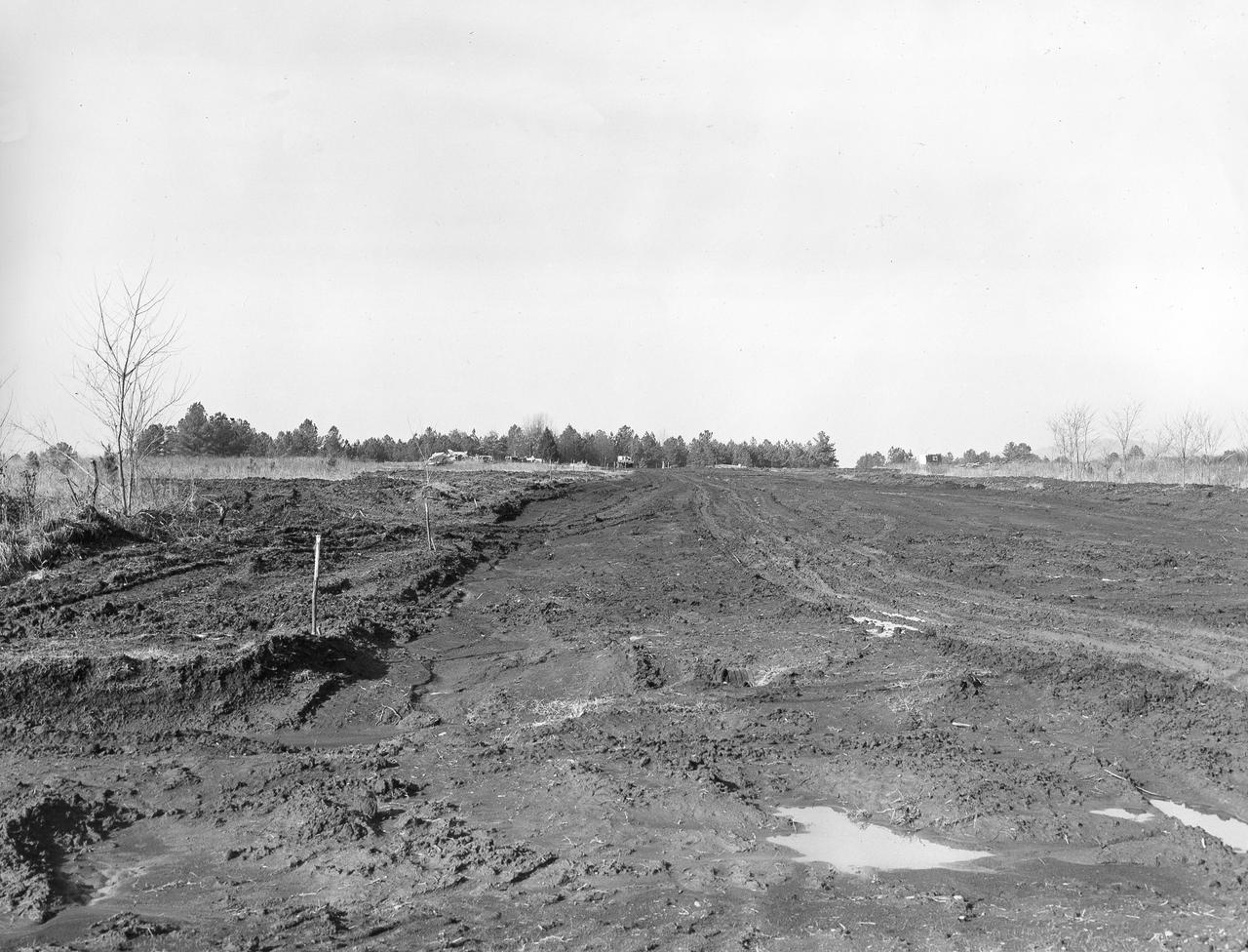 At its founding, the Marshall Space Flight Center (MSFC) inherited the Army’s Jupiter and Redstone test stands, but much larger facilities were needed for the giant stages of the Saturn V. From 1960 to 1964, the existing stands were remodeled and a sizable new test area was developed. The new comprehensive test complex for propulsion and structural dynamics was unique within the nation and the free world, and they remain so today because they were constructed with foresight to meet the future as well as on going needs. Construction of the S-IC Static test stand complex began in 1961 in the west test area of MSFC, and was completed in 1964. The S-IC static test stand was designed to develop and test the 138-ft long and 33-ft diameter Saturn V S-IC first stage, or booster stage, weighing in at 280,000 pounds. Required to hold down the brute force of a 7,500,000-pound thrust produced by 5 F-1 engines, the S-IC static test stand was designed and constructed with the strength of hundreds of tons of steel and 12,000,000 pounds of cement, planted down to bedrock 40 feet below ground level. The foundation walls, constructed with concrete and steel, are 4 feet thick. The base structure consists of four towers with 40-foot-thick walls extending upward 144 feet above ground level. The structure was topped by a crane with a 135-foot boom. With the boom in the upright position, the stand was given an overall height of 405 feet, placing it among the highest structures in Alabama at the time. In addition to the stand itself, related facilities were constructed during this time. Built directly east of the test stand was the Block House, which served as the control center for the test stand. The two were connected by a narrow access tunnel which housed the cables for the controls.  This photo, taken January 23, 1962, shows the excavation of the Block House site. 