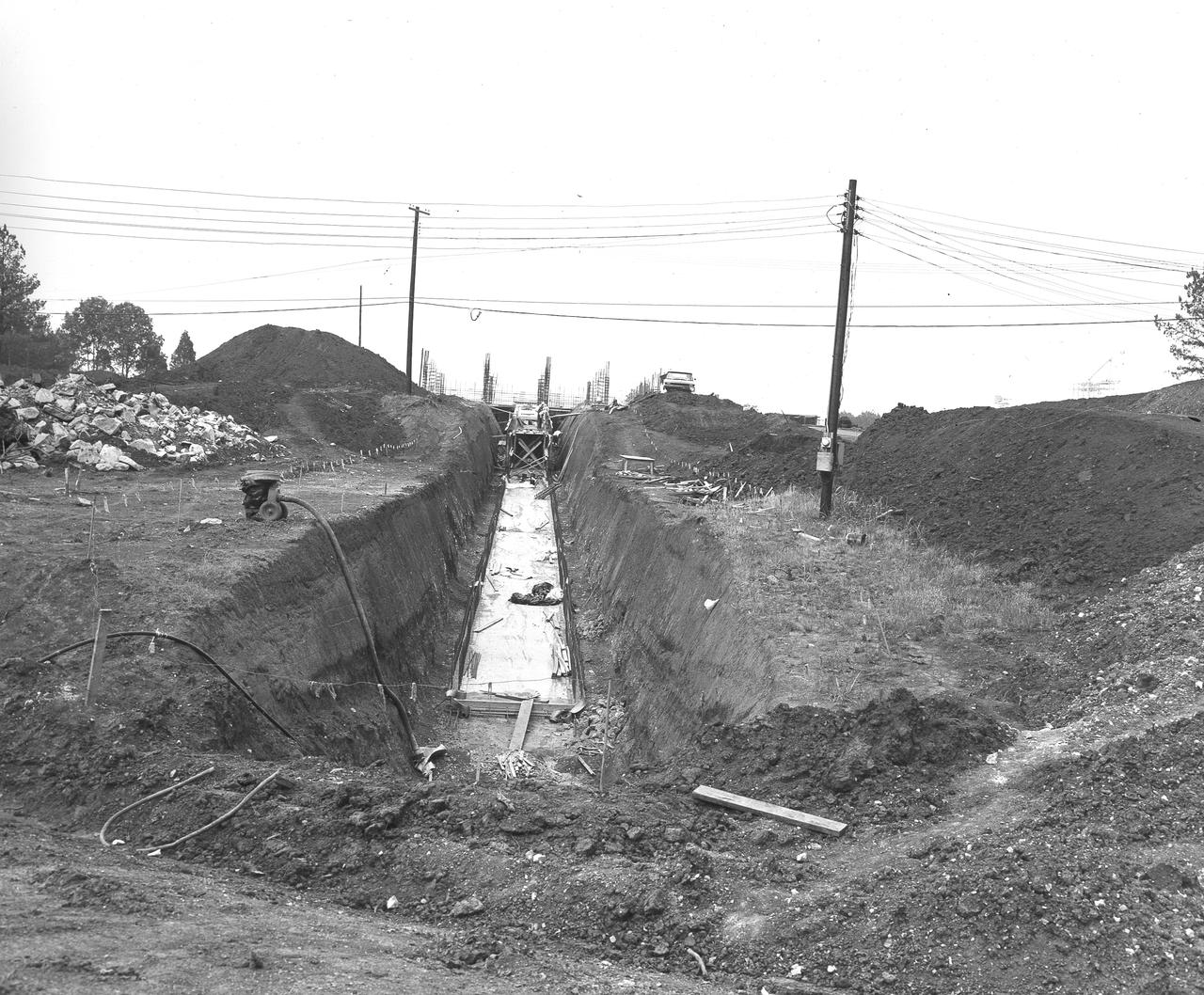 At its founding, the Marshall Space Flight Center (MSFC) inherited the Army’s Jupiter and Redstone test stands, but much larger facilities were needed for the giant stages of the Saturn V. From 1960 to 1964, the existing stands were remodeled and a sizable new test area was developed. The new comprehensive test complex for propulsion and structural dynamics was unique within the nation and the free world, and they remain so today because they were constructed with foresight to meet the future as well as on going needs. Construction of the S-IC Static test stand complex began in 1961 in the west test area of MSFC, and was completed in 1964. The S-IC static test stand was designed to develop and test the 138-ft long and 33-ft diameter Saturn V S-IC first stage, or booster stage, weighing in at 280,000 pounds. Required to hold down the brute force of a 7,500,000-pound thrust produced by 5 F-1 engines, the S-IC static test stand was designed and constructed with the strength of hundreds of tons of steel and 12,000,000 pounds of cement, planted down to bedrock 40 feet below ground level. The foundation walls, constructed with concrete and steel, are 4 feet thick. The base structure consists of four towers with 40-foot-thick walls extending upward 144 feet above ground level. The structure was topped by a crane with a 135-foot boom. With the boom in the upright position, the stand was given an overall height of 405 feet, placing it among the highest structures in Alabama at the time. In addition to the stand itself, related facilities were constructed during this time. Built directly east of the test stand was the Block House, which served as the control center for the test stand. The two were connected by a narrow tunnel which housed the cables for the controls. This photograph, taken on May 21, 1962 depicts the access tunnel construction.