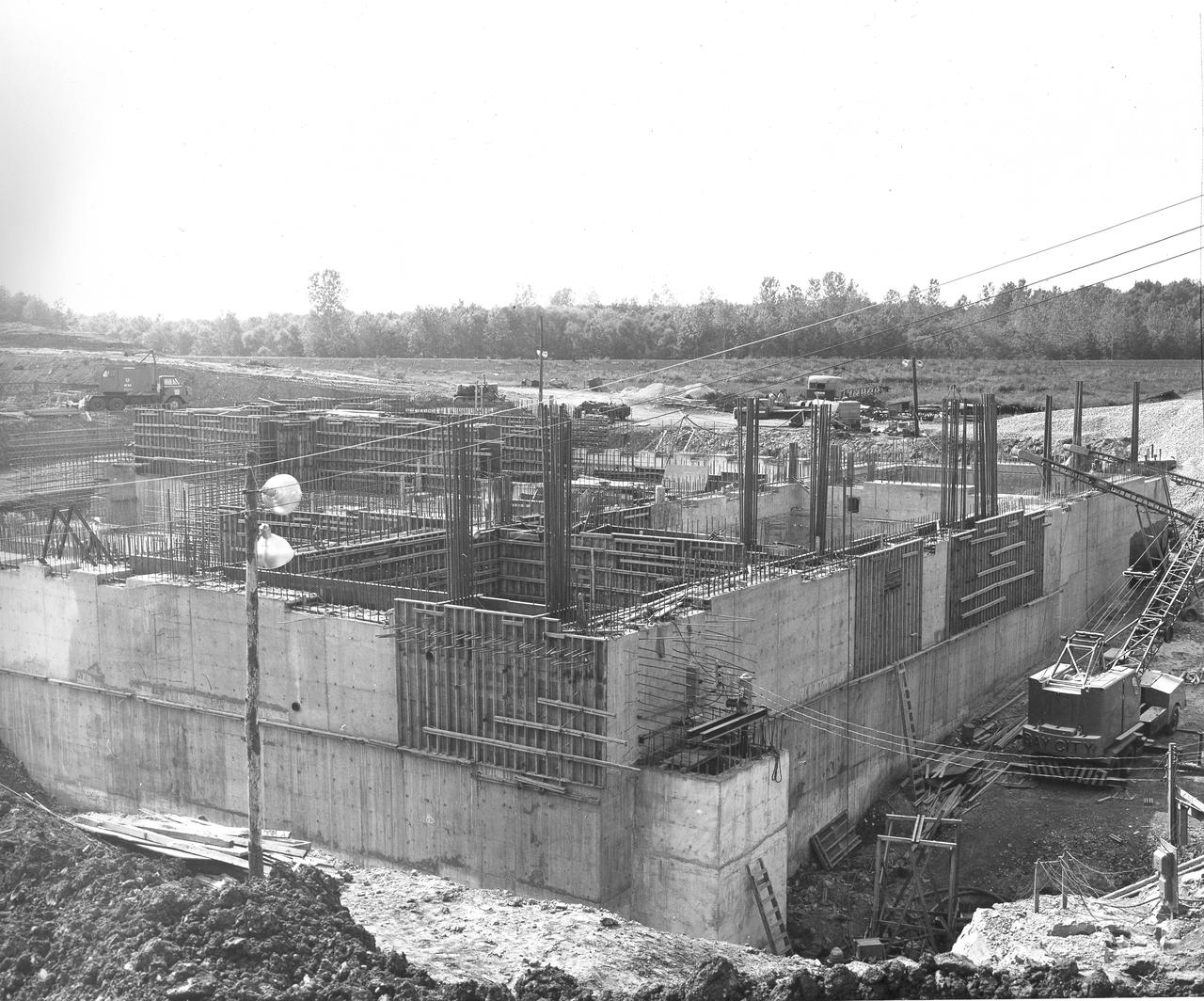 At its founding, the Marshall Space Flight Center (MSFC) inherited the Army’s Jupiter and Redstone test stands, but much larger facilities were needed for the giant stages of the Saturn V. From 1960 to 1964, the existing stands were remodeled and a sizable new test area was developed. The new comprehensive test complex for propulsion and structural dynamics was unique within the nation and the free world, and they remain so today because they were constructed with foresight to meet the future as well as on going needs. Construction of the S-IC Static test stand complex began in 1961 in the west test area of MSFC, and was completed in 1964. The S-IC static test stand was designed to develop and test the 138-ft long and 33-ft diameter Saturn V S-IC first stage, or booster stage, weighing in at 280,000 pounds. Required to hold down the brute force of a 7,500,000-pound thrust produced by 5 F-1 engines, the S-IC static test stand was designed and constructed with the strength of hundreds of tons of steel and 12,000,000 pounds of cement, planted down to bedrock 40 feet below ground level. The foundation walls, constructed with concrete and steel, are 4 feet thick. The base structure consists of four towers with 40-foot-thick walls extending upward 144 feet above ground level. The structure was topped by a crane with a 135-foot boom. With the boom in the upright position, the stand was given an overall height of 405 feet, placing it among the highest structures in Alabama at the time. In addition to the stand itself, related facilities were constructed during this time. Built directly east of the test stand was the Block House, which served as the control center for the test stand. The two were connected by a narrow access tunnel which housed the cables for the controls. This construction photo taken August 17, 1962 depicts a back side view of the Block House.