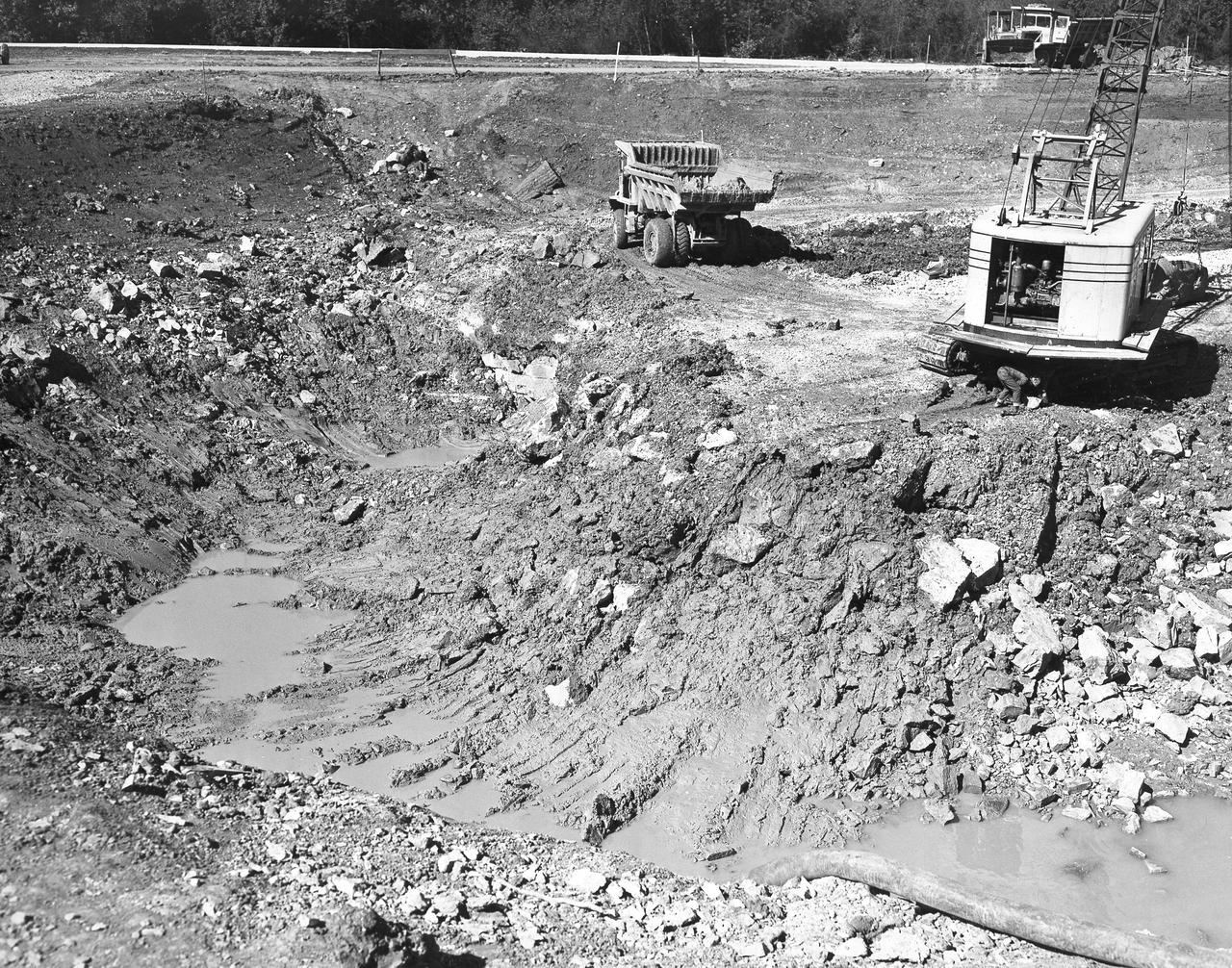 At its founding, the Marshall Space Flight Center (MSFC) inherited the Army’s Jupiter and Redstone test stands, but much larger facilities were needed for the giant stages of the Saturn V. From 1960 to 1964, the existing stands were remodeled and a sizable new test area was developed. The new comprehensive test complex for propulsion and structural dynamics was unique within the nation and the free world, and they remain so today because they were constructed with foresight to meet the future as well as on going needs. Construction of the S-IC Static test stand complex began in 1961 in the west test area of MSFC, and was completed in 1964. The S-IC static test stand was designed to develop and test the 138-ft long and 33-ft diameter Saturn V S-IC first stage, or booster stage, weighing in at 280,000 pounds. Required to hold down the brute force of a 7,500,000-pound thrust produced by 5 F-1 engines, the S-IC static test stand was designed and constructed with the strength of hundreds of tons of steel and 12,000,000 pounds of cement, planted down to bedrock 40 feet below ground level. The foundation walls, constructed with concrete and steel, are 4 feet thick. The base structure consists of four towers with 40-foot-thick walls extending upward 144 feet above ground level. The structure was topped by a crane with a 135-foot boom. With the boom in the upright position, the stand was given an overall height of 405 feet, placing it among the highest structures in Alabama at the time. In addition to the S-IC test stand, related  facilities were built during this time. Built to the north of the massive S-IC test stand, was the F-1 Engine test stand. The F-1 test stand, a vertical engine firing test stand, 239 feet in elevation and 4,600 square feet in area at the base, was designed to assist in the development of the F-1 Engine. Capability was provided for static firing of 1.5 million pounds of thrust using liquid oxygen and kerosene. Like the S-IC stand, the foundation of the F-1 stand is keyed into the bedrock approximately 40 feet below grade. This photo, taken October 26, 1962, depicts the excavation process of the single engine F-1 stand.