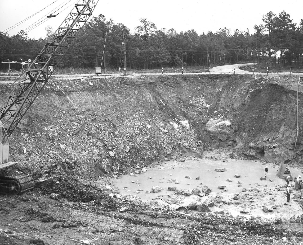 At its founding, the Marshall Space Flight Center (MSFC) inherited the Army’s Jupiter and Redstone test stands, but much larger facilities were needed for the giant stages of the Saturn V. From 1960 to 1964, the existing stands were remodeled and a sizable new test area was developed. The new comprehensive test complex for propulsion and structural dynamics was unique within the nation and the free world, and they remain so today because they were constructed with foresight to meet the future as well as on going needs. Construction of the S-IC Static test stand complex began in 1961 in the west test area of MSFC, and was completed in 1964. The S-IC static test stand was designed to develop and test the 138-ft long and 33-ft diameter Saturn V S-IC first stage, or booster stage, weighing in at 280,000 pounds. Required to hold down the brute force of a 7,500,000-pound thrust produced by 5 F-1 engines, the S-IC static test stand was designed and constructed with the strength of hundreds of tons of steel and 12,000,000 pounds of cement, planted down to bedrock 40 feet below ground level. The foundation walls, constructed with concrete and steel, are 4 feet thick. The base structure consists of four towers with 40-foot-thick walls extending upward 144 feet above ground level. The structure was topped by a crane with a 135-foot boom. With the boom in the upright position, the stand was given an overall height of 405 feet, placing it among the highest structures in Alabama at the time. In addition to the S-IC test stand, related  facilities were built during this time. Built to the north of the massive S-IC test stand, was the F-1 Engine test stand. The F-1 test stand, a vertical engine firing test stand, 239 feet in elevation and 4,600 square feet in area at the base, was designed to assist in the development of the F-1 Engine. Capability was provided for static firing of 1.5 million pounds of thrust using liquid oxygen and kerosene. Like the S-IC stand, the foundation of the F-1 stand is keyed into the bedrock approximately 40 feet below grade. This photo, taken November 15, 1962, depicts the excavation process of the single engine F-1 stand site.