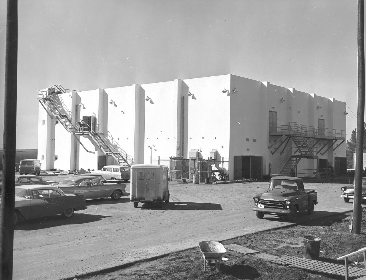 At its founding, the Marshall Space Flight Center (MSFC) inherited the Army’s Jupiter and Redstone test stands, but much larger facilities were needed for the giant stages of the Saturn V. From 1960 to 1964, the existing stands were remodeled and a sizable new test area was developed. The new comprehensive test complex for propulsion and structural dynamics was unique within the nation and the free world, and they remain so today because they were constructed with foresight to meet the future as well as on going needs. Construction of the S-IC Static test stand complex began in 1961 in the west test area of MSFC, and was completed in 1964. The S-IC static test stand was designed to develop and test the 138-ft long and 33-ft diameter Saturn V S-IC first stage, or booster stage, weighing in at 280,000 pounds. Required to hold down the brute force of a 7,500,000-pound thrust produced by 5 F-1 engines, the S-IC static test stand was designed and constructed with the strength of hundreds of tons of steel and 12,000,000 pounds of cement, planted down to bedrock 40 feet below ground level. The foundation walls, constructed with concrete and steel, are 4 feet thick. The base structure consists of four towers with 40-foot-thick walls extending upward 144 feet above ground level. The structure was topped by a crane with a 135-foot boom. With the boom in the upright position, the stand was given an overall height of 405 feet, placing it among the highest structures in Alabama at the time. In addition to the stand itself, related facilities were constructed during this time. Built directly east of the test stand was the Block House, which served as the control center for the test stand. The two were connected by a narrow access tunnel which housed the cables for the controls. In this photo taken February 4, 1963, the Block House exterior is complete.
