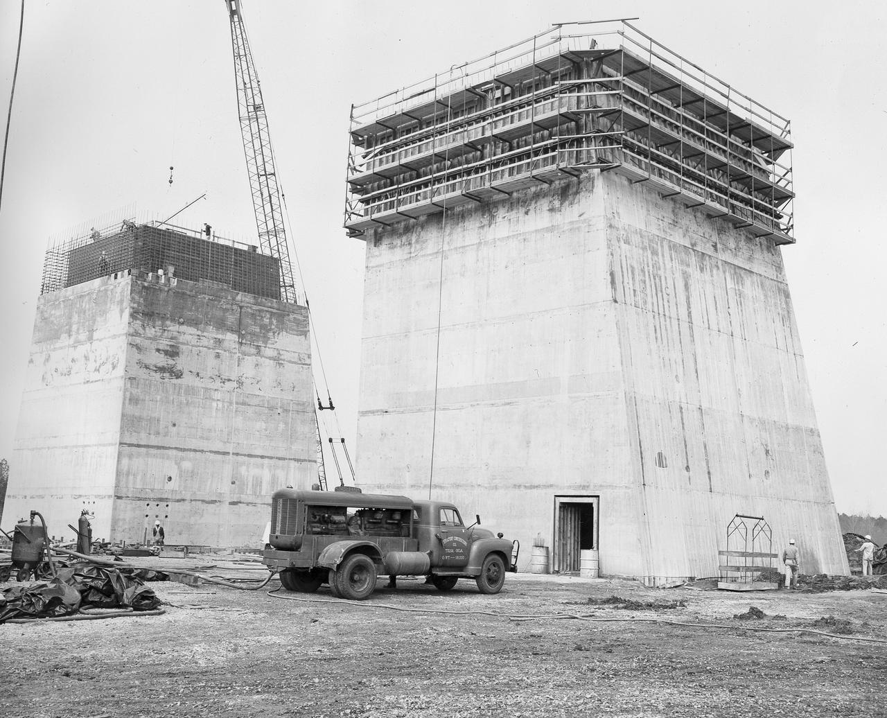 At its founding, the Marshall Space Flight Center (MSFC) inherited the Army’s Jupiter and Redstone test stands, but much larger facilities were needed for the giant stages of the Saturn V. From 1960 to 1964, the existing stands were remodeled and a sizable new test area was developed. The new comprehensive test complex for propulsion and structural dynamics was unique within the nation and the free world, and they remain so today because they were constructed with foresight to meet the future as well as on going needs. Construction of the S-IC Static test stand complex began in 1961 in the west test area of MSFC, and was completed in 1964. The S-IC static test stand was designed to develop and test the 138-ft long and 33-ft diameter Saturn V S-IC first stage, or booster stage, weighing in at 280,000 pounds. Required to hold down the brute force of a 7,500,000-pound thrust produced by 5 F-1 engines, the S-IC static test stand was designed and constructed with the strength of hundreds of tons of steel and 12,000,000 pounds of cement, planted down to bedrock 40 feet below ground level. The foundation walls, constructed with concrete and steel, are 4 feet thick. The base structure consists of four towers with 40-foot-thick walls extending upward 144 feet above ground level. The structure was topped by a crane with a 135-foot boom. With the boom in the upright position, the stand was given an overall height of 405 feet, placing it among the highest structures in Alabama at the time. This photograph taken March 29, 1963, gives a close up look at two of the ever-growing four towers of the S-IC Test Stand.