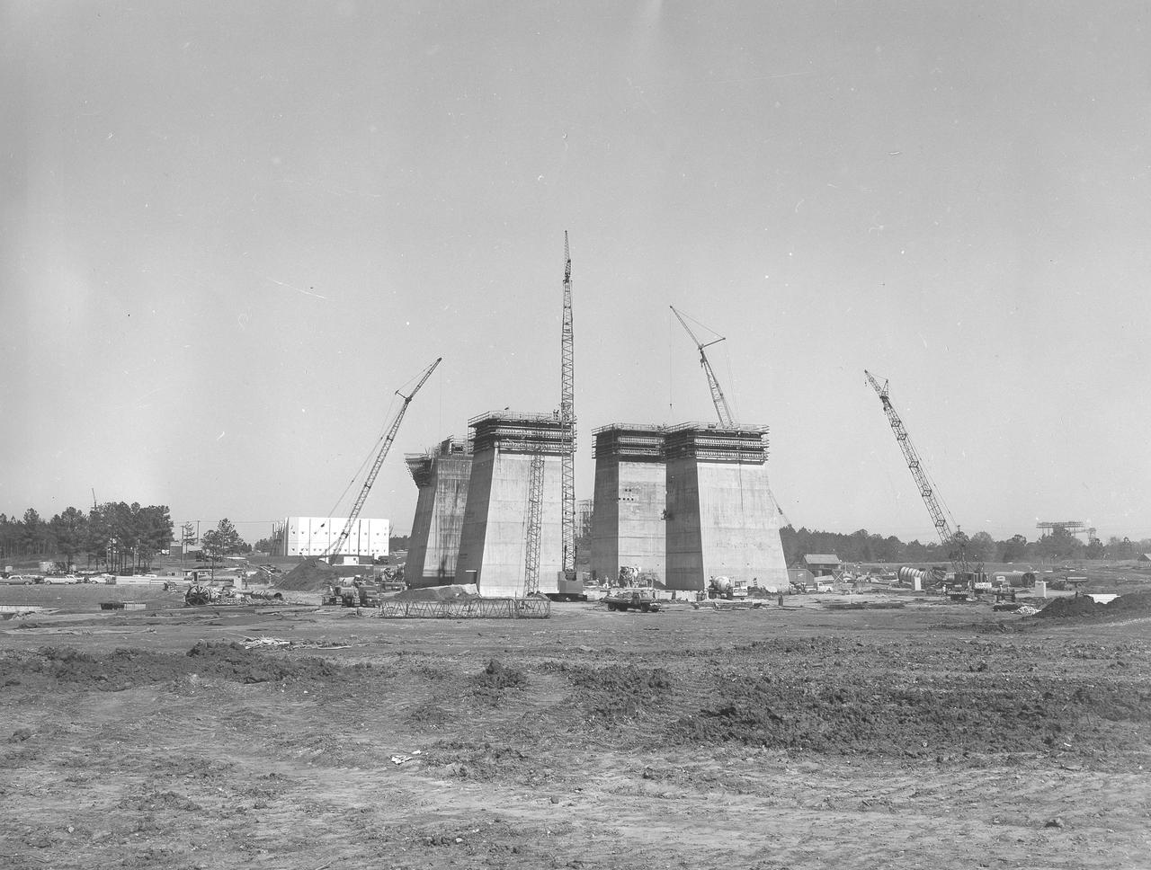 At its founding, the Marshall Space Flight Center (MSFC) inherited the Army’s Jupiter and Redstone test stands, but much larger facilities were needed for the giant stages of the Saturn V. From 1960 to 1964, the existing stands were remodeled and a sizable new test area was developed. The new comprehensive test complex for propulsion and structural dynamics was unique within the nation and the free world, and they remain so today because they were constructed with foresight to meet the future as well as on going needs. Construction of the S-IC Static test stand complex began in 1961 in the west test area of MSFC, and was completed in 1964. The S-IC static test stand was designed to develop and test the 138-ft long and 33-ft diameter Saturn V S-IC first stage, or booster stage, weighing in at 280,000 pounds. Required to hold down the brute force of a 7,500,000-pound thrust produced by 5 F-1 engines, the S-IC static test stand was designed and constructed with the strength of hundreds of tons of steel and 12,000,000 pounds of cement, planted down to bedrock 40 feet below ground level. The foundation walls, constructed with concrete and steel, are 4 feet thick. The base structure consists of four towers with 40-foot-thick walls extending upward 144 feet above ground level. The structure was topped by a crane with a 135-foot boom. With the boom in the upright position, the stand was given an overall height of 405 feet, placing it among the highest structures in Alabama at the time. This photograph, taken April 4, 1963, gives a close up look at the ever-growing four towers of the S-IC Test Stand.