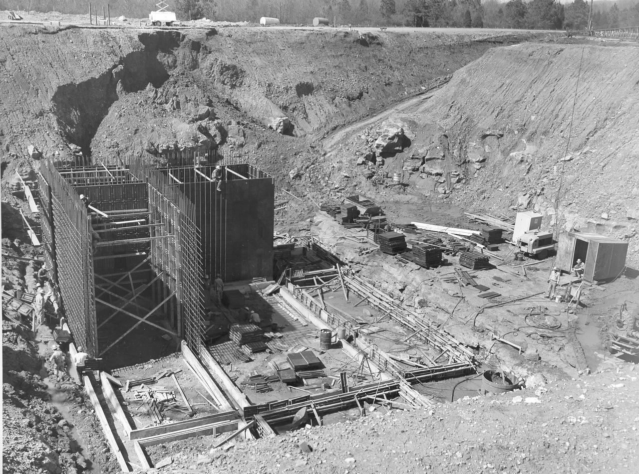At its founding, the Marshall Space Flight Center (MSFC) inherited the Army’s Jupiter and Redstone test stands, but much larger facilities were needed for the giant stages of the Saturn V. From 1960 to 1964, the existing stands were remodeled and a sizable new test area was developed. The new comprehensive test complex for propulsion and structural dynamics was unique within the nation and the free world, and they remain so today because they were constructed with foresight to meet the future as well as on going needs. Construction of the S-IC Static test stand complex began in 1961 in the west test area of MSFC, and was completed in 1964. The S-IC static test stand was designed to develop and test the 138-ft long and 33-ft diameter Saturn V S-IC first stage, or booster stage, weighing in at 280,000 pounds. Required to hold down the brute force of a 7,500,000-pound thrust produced by 5 F-1 engines, the S-IC static test stand was designed and constructed with the strength of hundreds of tons of steel and 12,000,000 pounds of cement, planted down to bedrock 40 feet below ground level. The foundation walls, constructed with concrete and steel, are 4 feet thick. The base structure consists of four towers with 40-foot-thick walls extending upward 144 feet above ground level. The structure was topped by a crane with a 135-foot boom. With the boom in the upright position, the stand was given an overall height of 405 feet, placing it among the highest structures in Alabama at the time. North of the massive S-IC test stand, the F-1 Engine test stand was built. Designed to assist in the development of the F-1 Engine, the F-1 test stand is a vertical engine firing test stand, 239 feet in elevation and 4,600 square feet in area at the base. Capability was provided for static firing of 1.5 million pounds of thrust using liquid oxygen and kerosene. Like the S-IC stand, the foundation of the F-1 stand is keyed into the bedrock approximately 40 feet below grade. This photo, taken April 4, 1963 depicts the construction of the F-1 test stand foundation walls.