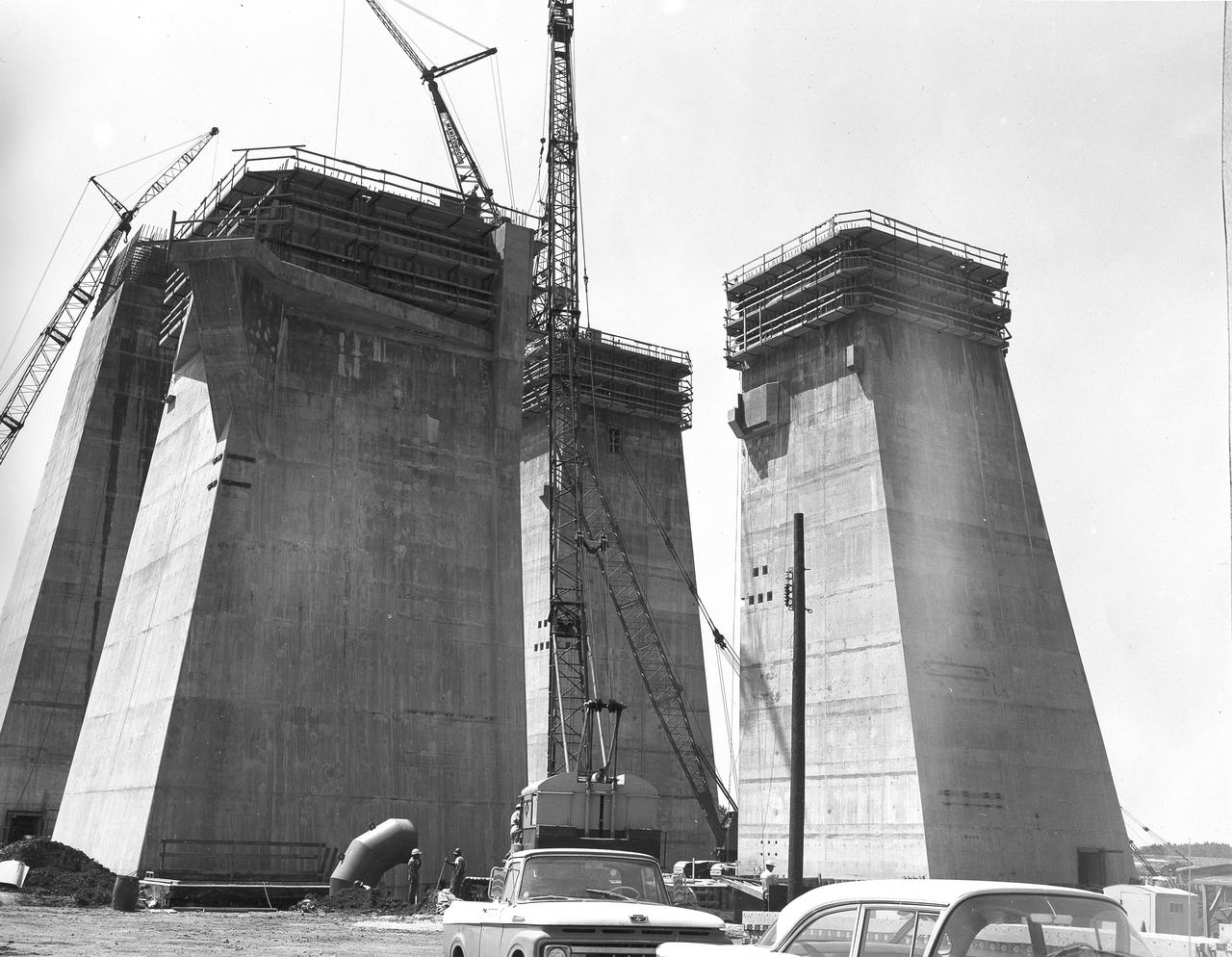 At its founding, the Marshall Space Flight Center (MSFC) inherited the Army’s Jupiter and Redstone test stands, but much larger facilities were needed for the giant stages of the Saturn V. From 1960 to 1964, the existing stands were remodeled and a sizable new test area was developed. The new comprehensive test complex for propulsion and structural dynamics was unique within the nation and the free world, and they remain so today because they were constructed with foresight to meet the future as well as on going needs. Construction of the S-IC Static test stand complex began in 1961 in the west test area of MSFC, and was completed in 1964. The S-IC static test stand was designed to develop and test the 138-ft long and 33-ft diameter Saturn V S-IC first stage, or booster stage, weighing in at 280,000 pounds. Required to hold down the brute force of a 7,500,000-pound thrust produced by 5 F-1 engines, the S-IC static test stand was designed and constructed with the strength of hundreds of tons of steel and 12,000,000 pounds of cement, planted down to bedrock 40 feet below ground level. The foundation walls, constructed with concrete and steel, are 4 feet thick. The base structure consists of four towers with 40-foot-thick walls extending upward 144 feet above ground level. The structure was topped by a crane with a 135-foot boom. With the boom in the upright position, the stand was given an overall height of 405 feet, placing it among the highest structures in Alabama at the time. This photograph, taken May 7, 1963, gives a close look at the four concrete tower legs of the S-IC test stand at their completed height.