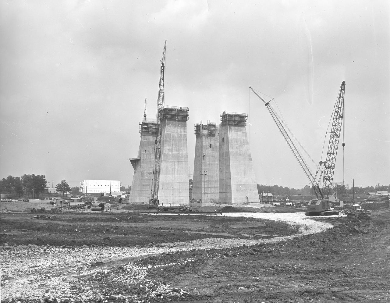 At its founding, the Marshall Space Flight Center (MSFC) inherited the Army’s Jupiter and Redstone test stands, but much larger facilities were needed for the giant stages of the Saturn V. From 1960 to 1964, the existing stands were remodeled and a sizable new test area was developed. The new comprehensive test complex for propulsion and structural dynamics was unique within the nation and the free world, and they remain so today because they were constructed with foresight to meet the future as well as on going needs. Construction of the S-IC Static test stand complex began in 1961 in the west test area of MSFC, and was completed in 1964. The S-IC static test stand was designed to develop and test the 138-ft long and 33-ft diameter Saturn V S-IC first stage, or booster stage, weighing in at 280,000 pounds. Required to hold down the brute force of a 7,500,000-pound thrust produced by 5 F-1 engines, the S-IC static test stand was designed and constructed with the strength of hundreds of tons of steel and 12,000,000 pounds of cement, planted down to bedrock 40 feet below ground level. The foundation walls, constructed with concrete and steel, are 4 feet thick. The base structure consists of four towers with 40-foot-thick walls extending upward 144 feet above ground level. The structure was topped by a crane with a 135-foot boom. With the boom in the upright position, the stand was given an overall height of 405 feet, placing it among the highest structures in Alabama at the time. In this photo, taken June 24, 1963, the four tower legs of the test stand can be seen at their maximum height.
