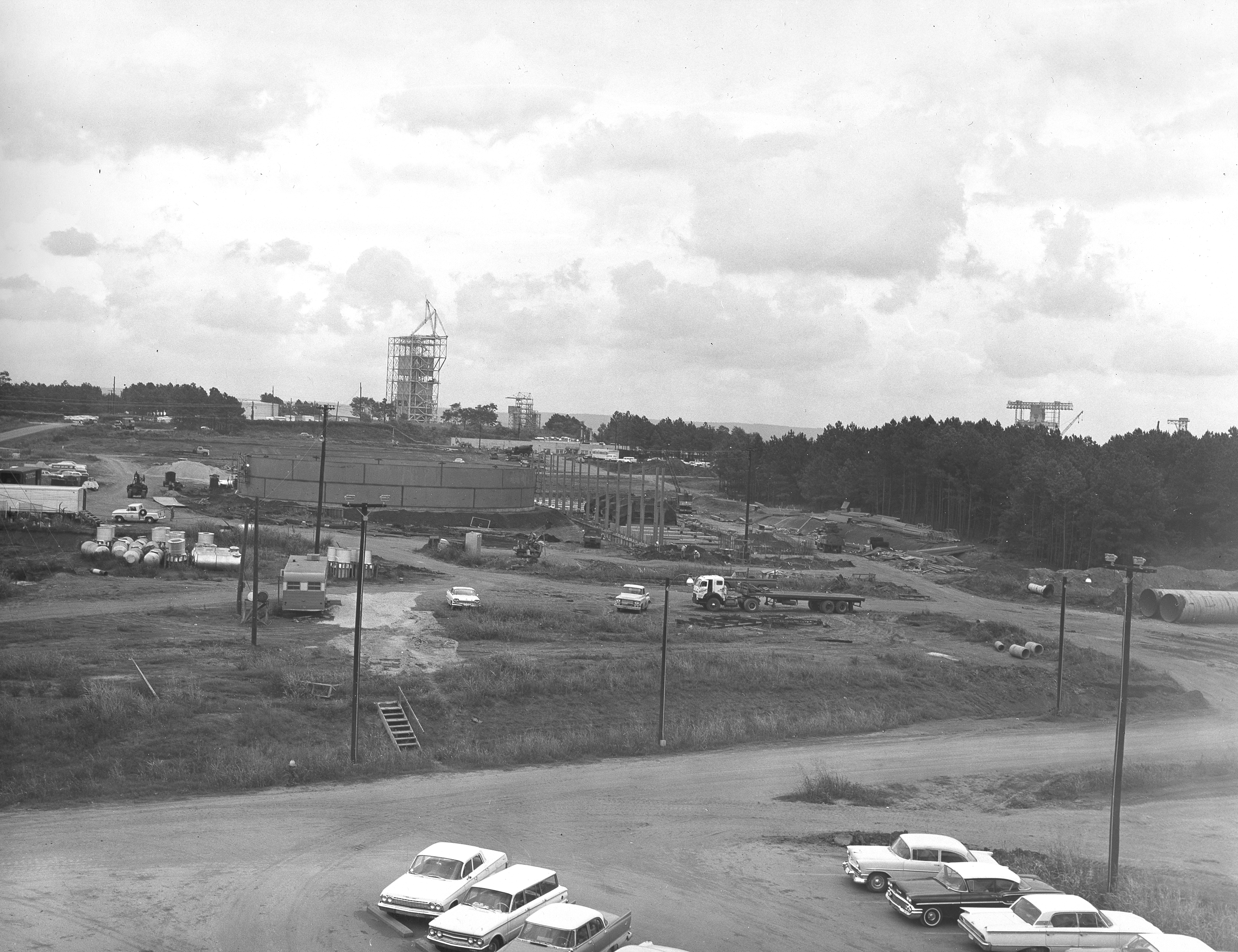 At its founding, the Marshall Space Flight Center (MSFC) inherited the Army’s Jupiter and Redstone test stands, but much larger facilities were needed for the giant stages of the Saturn V. From 1960 to 1964, the existing stands were remodeled and a sizable new test area was developed. The new comprehensive test complex for propulsion and structural dynamics was unique within the nation and the free world, and they remain so today because they were constructed with foresight to meet the future as well as on going needs. Construction of the S-IC Static test stand complex began in 1961 in the west test area of MSFC, and was completed in 1964. The S-IC static test stand was designed to develop and test the 138-ft long and 33-ft diameter Saturn V S-IC first stage, or booster stage, weighing in at 280,000 pounds. Required to hold down the brute force of a 7,500,000-pound thrust produced by 5 F-1 engines, the S-IC static test stand was designed and constructed with the strength of hundreds of tons of steel and 12,000,000 pounds of cement, planted down to bedrock 40 feet below ground level. The foundation walls, constructed with concrete and steel, are 4 feet thick. The base structure consists of four towers with 40-foot-thick walls extending upward 144 feet above ground level. The structure was topped by a crane with a 135-foot boom. With the boom in the upright position, the stand was given an overall height of 405 feet, placing it among the highest structures in Alabama at the time. In addition to the stand itself, related facilities were constructed during this time. Built to the northeast east was a newly constructed Pump House. Its function was to provide water to the stand to prevent melting damage during testing. The water was sprayed through small holes in the stand’s 1900 ton flame deflector at the rate of 320,000 gallons per minute. This photograph of the Pump House area was taken August 13, 1963. The massive round water storage tanks can be seen to the left of the Pump House.