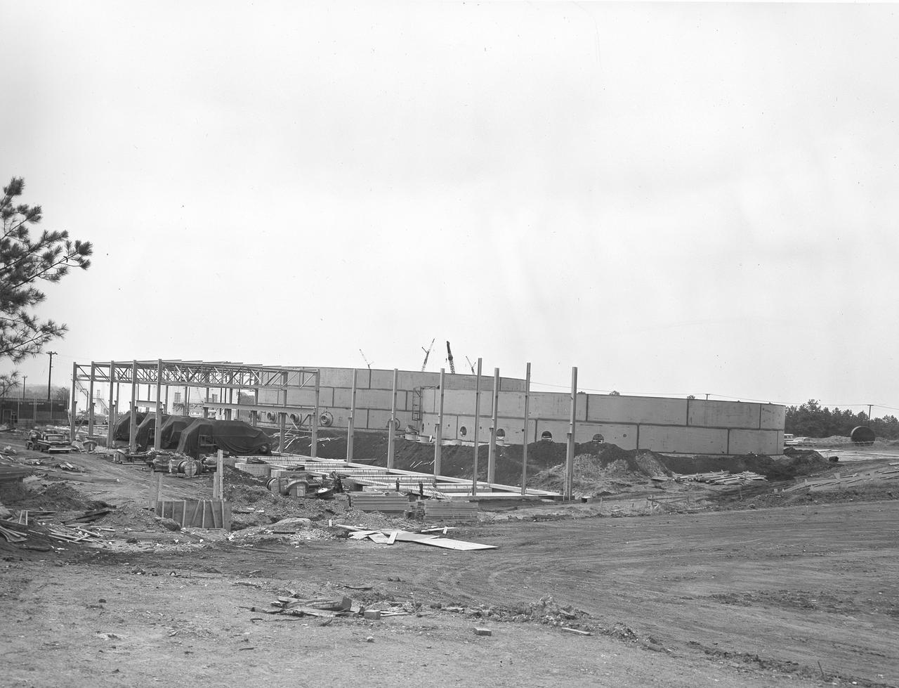 At its founding, the Marshall Space Flight Center (MSFC) inherited the Army’s Jupiter and Redstone test stands, but much larger facilities were needed for the giant stages of the Saturn V. From 1960 to 1964, the existing stands were remodeled and a sizable new test area was developed. The new comprehensive test complex for propulsion and structural dynamics was unique within the nation and the free world, and they remain so today because they were constructed with foresight to meet the future as well as on going needs. Construction of the S-IC Static test stand complex began in 1961 in the west test area of MSFC, and was completed in 1964. The S-IC static test stand was designed to develop and test the 138-ft long and 33-ft diameter Saturn V S-IC first stage, or booster stage, weighing in at 280,000 pounds. Required to hold down the brute force of a 7,500,000-pound thrust produced by 5 F-1 engines, the S-IC static test stand was designed and constructed with the strength of hundreds of tons of steel and 12,000,000 pounds of cement, planted down to bedrock 40 feet below ground level. The foundation walls, constructed with concrete and steel, are 4 feet thick. The base structure consists of four towers with 40-foot-thick walls extending upward 144 feet above ground level. The structure was topped by a crane with a 135-foot boom. With the boom in the upright position, the stand was given an overall height of 405 feet, placing it among the highest structures in Alabama at the time. In addition to the stand itself, related facilities were constructed during this time. Built to the northeast of the stand was a newly constructed Pump House. Its function was to provide water to the stand to prevent melting damage during testing. The water was sprayed through small holes in the stand’s 1900 ton flame deflector at the rate of 320,000 gallons per minute. This close up photograph, taken September 5, 1963, shows the ground level frame work for the Pump House and its massive round water storage tanks.
