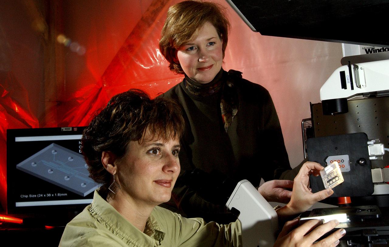 Helen Cole, the project manager for the Lab-on-a-Chip Applications Development program, and Lisa Monaco, the project scientist for the program, insert a lab on a chip into the Caliper 42 which is specialized equipment that controls processes on commercial chips to support development of lab-on-a-chip applications. The system has special microscopes and imaging systems, so scientists can process and study different types of fluid, chemical, and medical tests conducted on chips. For example, researchers have examined fluorescent bacteria as it flows through the chips' fluid channels or microfluidic capillaries. Researchers at NASA's Marshall Space Flight Center (MSFC) in Huntsville, Alabama, have been studying how the lab-on-a-chip technology can be used for microbial detection, water quality monitoring, and detecting biosignatures of past or present life on Mars. The Marshall Center team is also collaborating with scientists at other NASA centers and at universities to develop custom chip designs for not only space applications, but for many Earth applications, such as for detecting deadly microbes in heating and air systems. (NASA/MSFC/D.Stoffer)