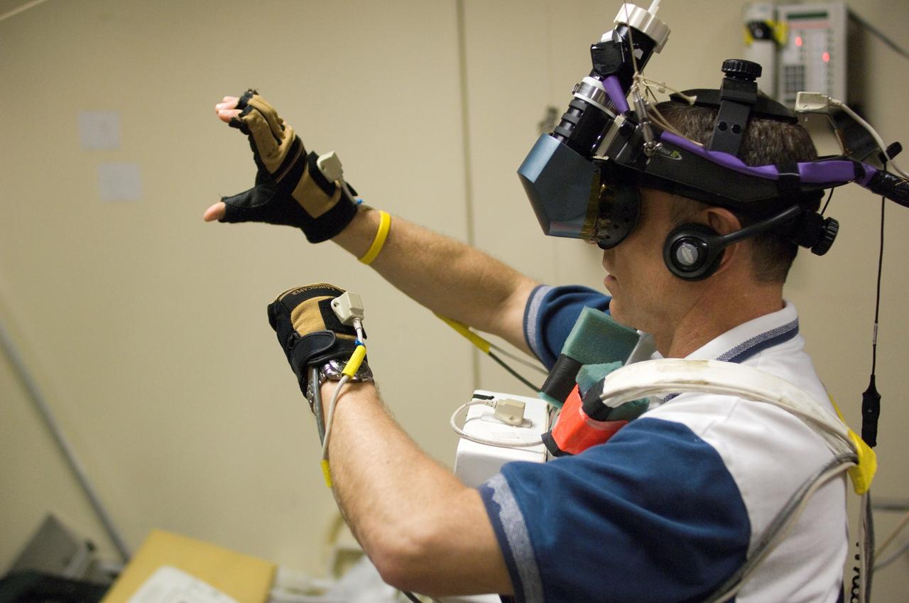 STS-118 astronaut and mission specialist Dafydd R. “Dave” Williams, representing the Canadian Space Agency, uses Virtual Reality Hardware in the Space Vehicle Mock Up Facility at the Johnson Space Center to rehearse some of his duties for the upcoming mission. This type of virtual reality training allows the astronauts to wear special gloves and other gear while looking at a computer that displays simulating actual movements around the various locations on the station hardware which with they will be working.