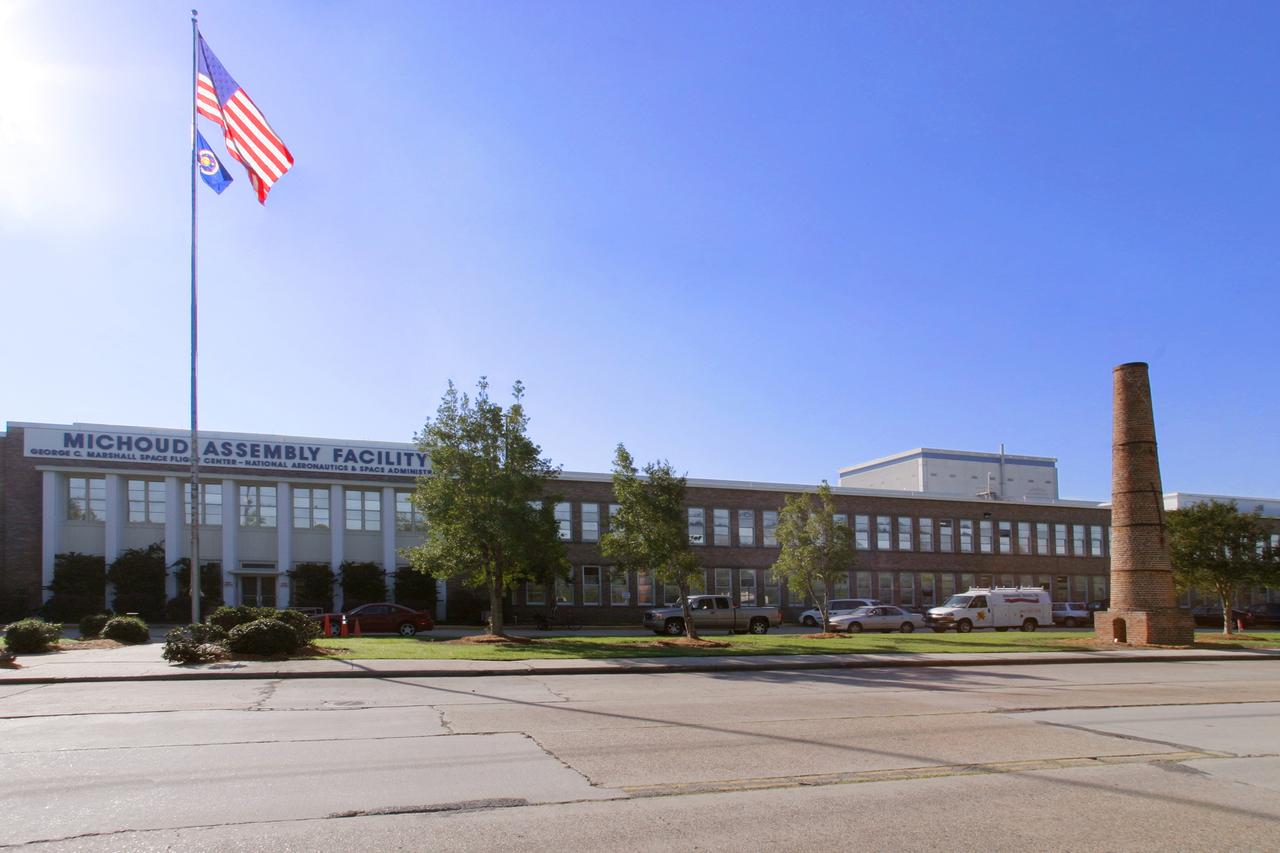 NASA's Michoud Assembly Facility, located in eastern New Orleans, Louisiana, is an 832 acre site that is a government-owned, contractor-operated component of the George C. Marshall Space Flight Center (MSFC). The facility was acquired by NASA in 1961 at the recommendation of Dr. Wernher von Braun and his rocket team in Huntsville Alabama. The cavernous plant served as the assembly facility for the Saturn launch vehicles and most recently the external tank (ET) used for the Space Shuttle Program. The facility features one of the world's biggest manufacturing plants with 43 acres under one roof and a port with deep-water access for the transportation of large space structures. When completed, space hardware is towed on a barge across the Gulf of Mexico, around Florida and up to Kennedy Space Center. The original tract of land was part of a 34,500 acre French Royal land grant to local merchant, Gilbert Antoine de St. Maxent in 1763. Later, the land was acquired by French transplant Antoine Michoud, the son of Napoleon's Administrator of Domains, who moved to the city in 1827. Michoud operated a sugar cane plantation and refinery on the site until his death in 1863. His heirs continued operating the refinery and kept the original St. Maxent estate intact into the 20th century. Visible on the right, is one of two brick smokestacks from the original refinery that still stand before the Michoud facility today.     