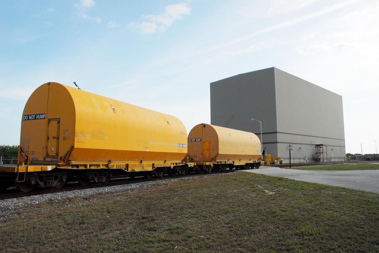 KENNEDY SPACE CENTER, FLA. --   The locomotive and rail cars carrying solid rocket booster motor segments and two aft exit cone segments roll toward the Rotation, Processing and Surge Facility (RPSF) in Kennedy Space Center's Launch Complex 39 Area.   The RPSF is used for solid rocket motor receiving, rotation and inspection, and supports aft booster buildup.  When live solid rocket motor segments arrive at the processing facility, they  are positioned under one of the cranes. Handling slings are then attached to and remove the railcar cover. The segment is inspected while it remains horizontal.  The two overhead cranes hoist the segment, rotate it to a vertical position and place it on a fixed stand. The aft handling ring is then removed. The segment is hoisted again and lowered onto a transportation and storage pallet, and the forward handling ring is removed to allow inspections. It is then transported to one of the surge buildings and temporarily stored until it is needed for booster stacking in the VAB.  While enroute, solid rocket motor segments were involved in a derailment in Alabama.  The rail cars carrying these segments remained upright and were undamaged.  An inspection determined these segment cars could continue on to Florida.  The segments themselves will undergo further evaluation at Kennedy before they are cleared for flight.  Other segments involved in the derailment will be returned to a plant in Utah for further evaluation.  Photo credit: NASA_George Shelton