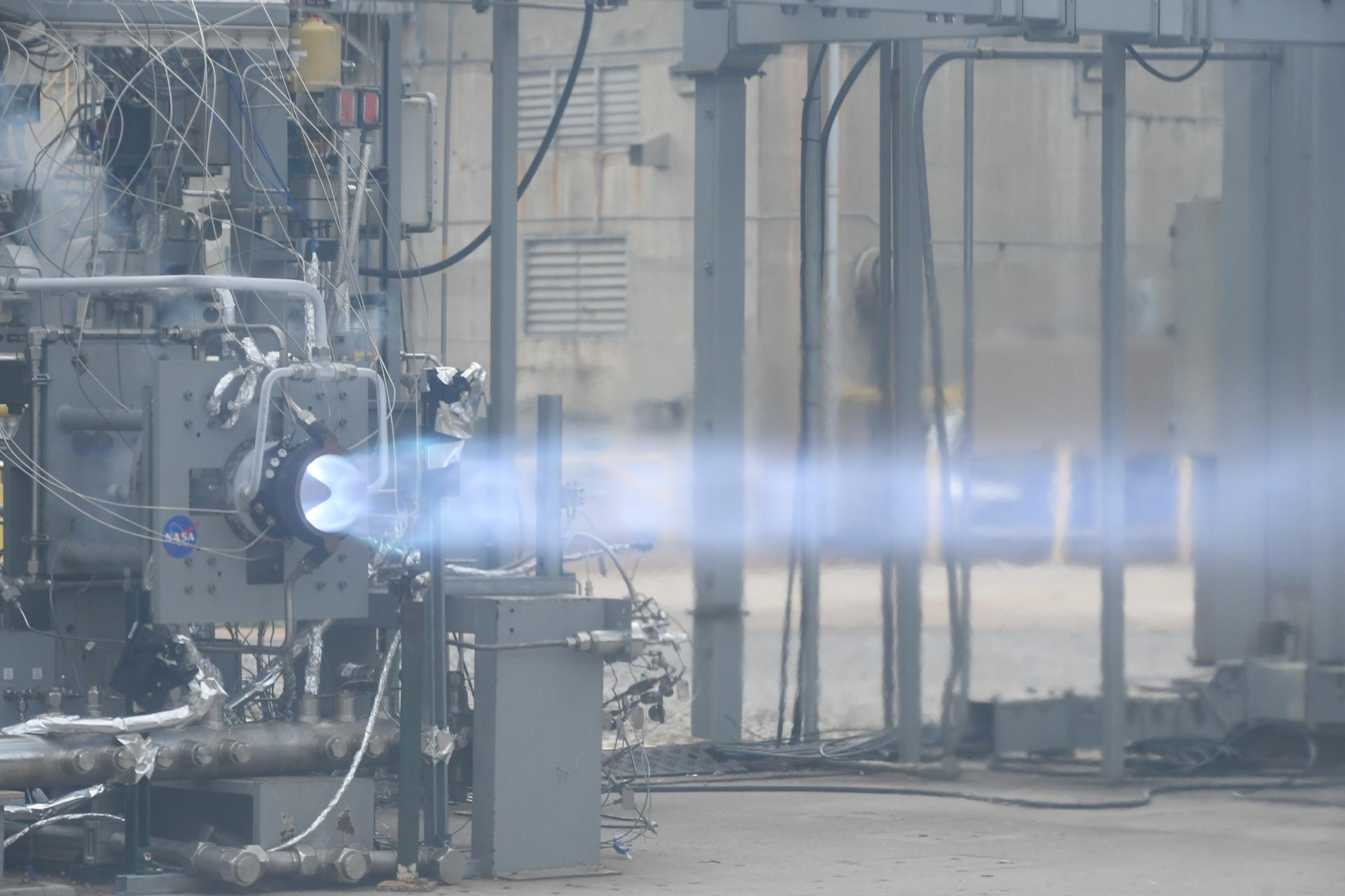A blue-white rotating detonation engine plume firing horizontally inside a test cell.