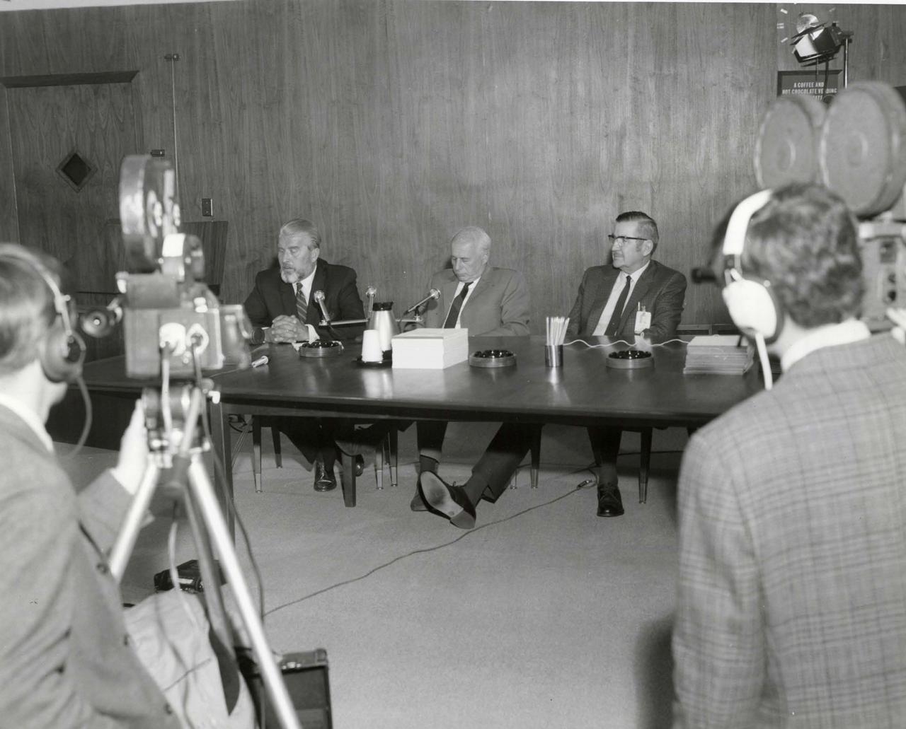 Dr. Wernher Von Braun, Dr. Eberhard Rees, and R.W. Cook at a press conference with cameras in the foreground.