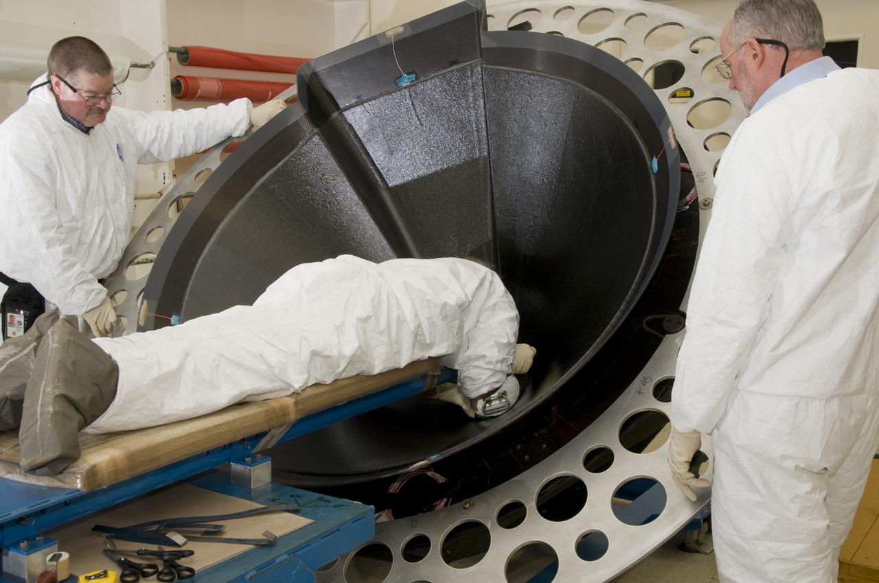 STEVE FRANKLIN, LEFT, AND RICHARD WELCH STAND READY TO ASSIST ED KIRSCH AS HE INSTALLS A ROUND PIECE OF COMPOSITE MATERIAL IN THE "BEANIE CAP" AT THE VERY TOP INSIDE THE COMPOSITE NOSE CONE.