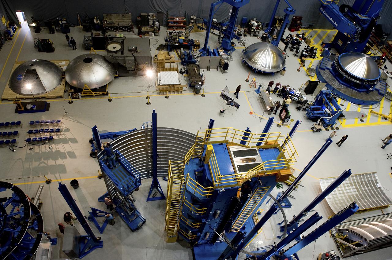 THE OVERHEAD VIEW OF THE FLOOR OF THE FRICTION STIR HIGH BAY AREA IN BUILDING 4755. THIS VIEW SHOWS FOUR DOME PIECES AS WELL AS THE SHELL BUCKLE BARREL PANEL IN THE VERTICAL WELD TOOL
