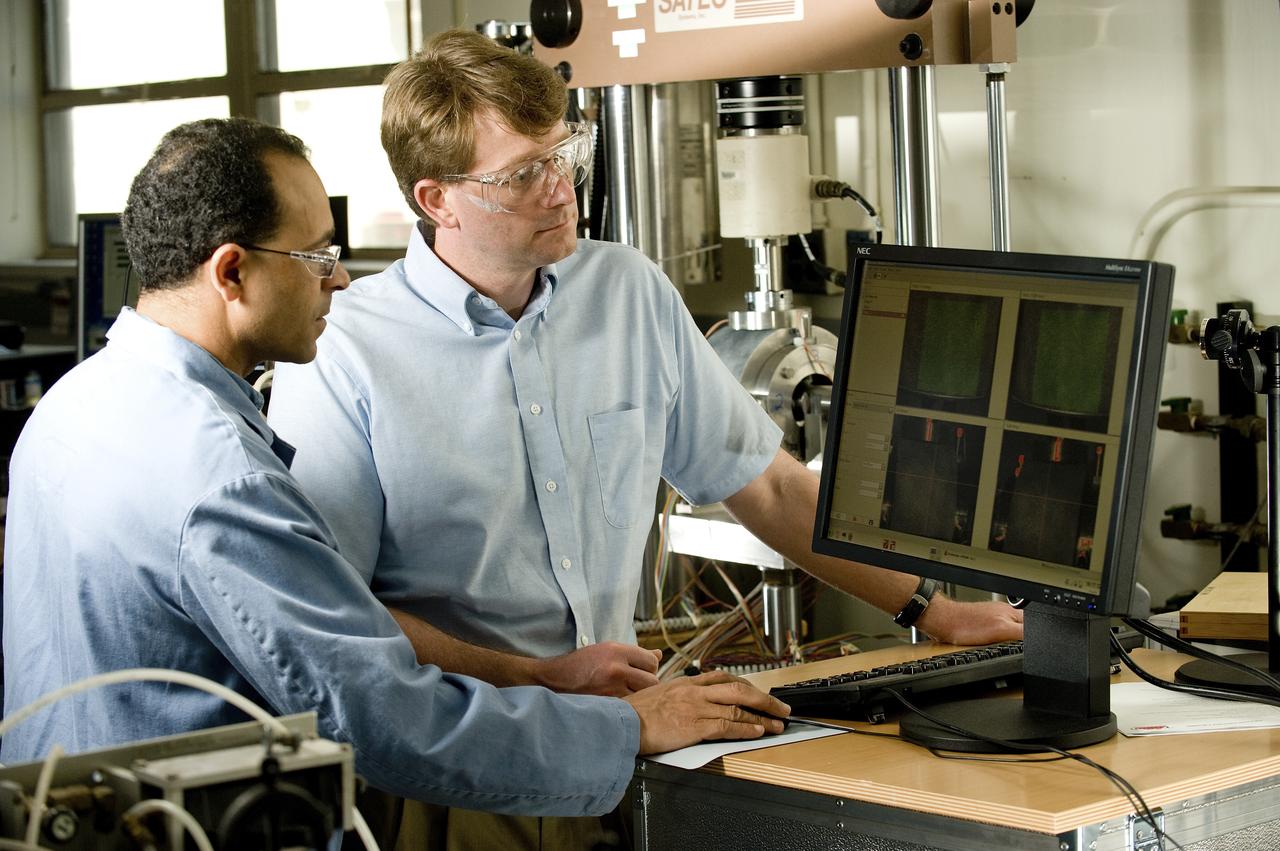 AYMAN GIRGIS (EM10 MATERIALS TEST ENGINEER, JACOBS ESTS GROUP/JTI) AND ERIC EARHART (AEROSPACE ENGINEER, ER41 PROPULSION STRUCTURAL & DYNAMICS ANALYSIS BRANCH) DISCUSS DATA PRODUCED BY A UNIQUE MECHANICAL TEST SETUP THAT MEASURES STRAIN ON A SINGLE SAMPLE, USING TWO DIFFERENT TECHNIQUES AT THE SAME TIME. THE TEST FIXTURE HOLDS A SPECIMEN THAT REPRESENTS A LIQUID OXYGEN (LOX) BEARING FROM THE J2-X ENGINE.