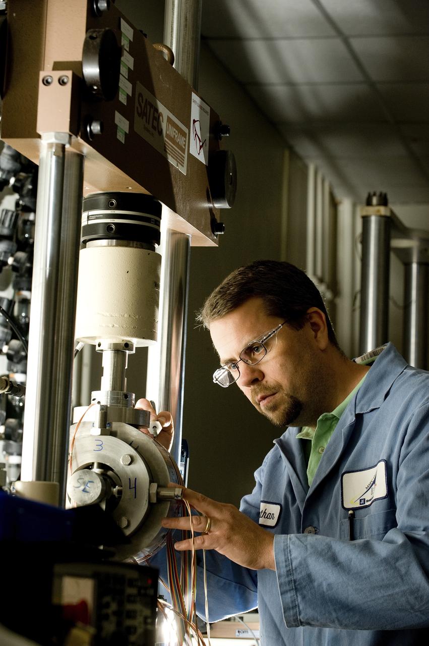 TATHAN COFFEE (EM10 MATERIALS TEST ENGINEER, JACOBS ESTS GROUP/JTI) ADJUSTS A UNIQUE MECHANICAL TEST SETUP THAT MEASURES STRAIN ON A SINGLE SAMPLE, USING TWO DIFFERENT TECHNIQUES AT THE SAME TIME. THE TEST FIXTURE HOLDS A SPECIMEN THAT REPRESENTS A LIQUID OXYGEN (LOX) BEARING FROM THE J2-X ENGINE