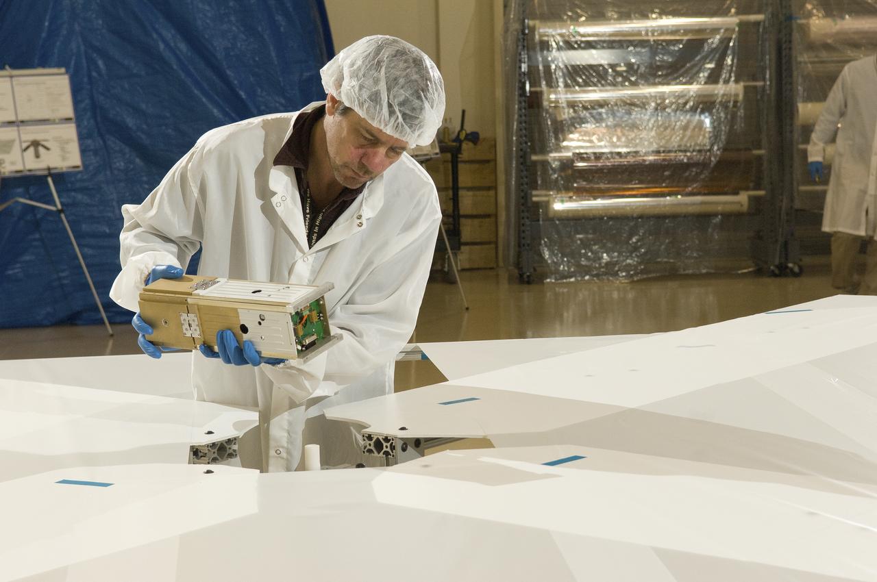 DOUG HUIE, RESEARCH TECHNICIAN AT THE UNIVERSITY OF ALABAMA IN HUNTSVILLE, CAFEFULLY SETS THE NANOSAIL-D SATELLITE ON A SPECIALLY CONSTRUCTED SURFACE DESIGNED FOR DEPLOYMENT TESTING. THE SPACECRAFT MEASURES 4 INCHES WIDE, 4 INCHES DEEP, AND 13 INCHES LONG, ROUGHLY THE SIZE OF A LOAF OF BREAD, AND WEIGHING ABOUT 9 POUNDS.