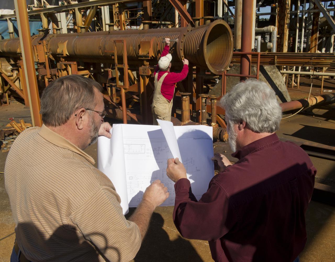 JEREMY KELLY, BACKGROUND, BEGINS DISASSEMBLING THE HOT GAS FACILITY'S WIND TUNNEL AS SCOOTER CLIFTON, FRONT LEFT, AND GREG VINYARD REVIEW THE FACILITY'S REDESIGN PLANS.