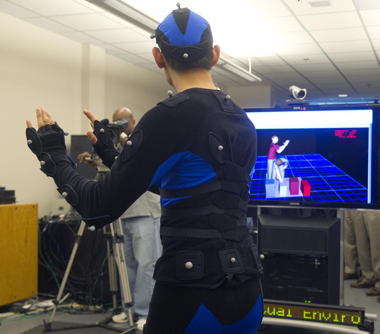 PETER MA, EV74, WEARS A SUIT COVERED WITH SPHERICAL REFLECTORS THAT ENABLE HIS MOTIONS TO BE TRACKED BY THE MOTION CAPTURE SYSTEM. THE HUMAN MODEL IN RED ON THE SCREEN IN THE BACKGROUND REPRESENTS THE SYSTEM-GENERATED IMAGE OF PETER'S POSITION.