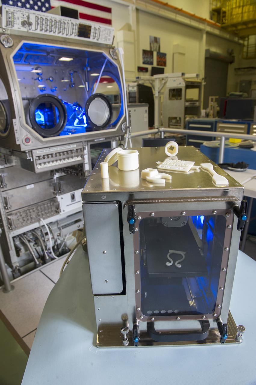 “MADE IS SPACE” 3D PRINTER IN FOREGROUND WITH MICROGRAVITY GLOVEBOX IN BACKGROUND, COVER PHOTO FOR NASA TECH BRIEFS MAGAZINE, JUNE 2014 ISSUE