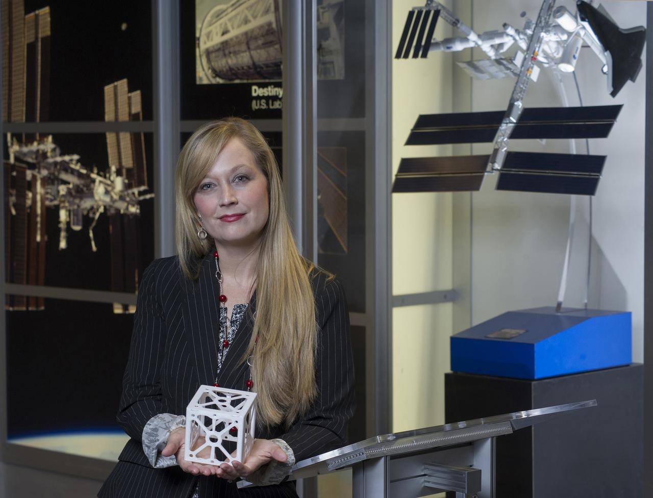 NIKI WERKHEISER, NASA'S 3D PRINTING IN ZERO-G PROJECT MANAGER, HOLDS A 3D PRINTED CUBESAT STRUCTURE WHICH IS JUST ONE OF THE MANY POTENTIAL APPLICATIONS THAT AN IN-SPACE MANUFACTURING CAPABILITY WILL PROVIDE
