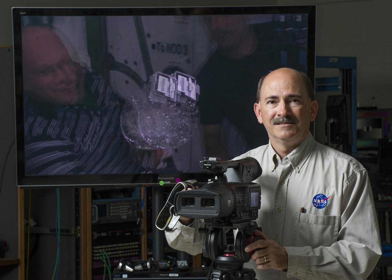 RODNEY GRUBBS, PROGRAM MANAGER FOR NASA'S IMAGERY EXPERTS PROGRAM AT THE MARSHALL SPACE FLIGHT CENTER, DISPLAYS THE 3-D CAMERA THAT WAS RETURNED FROM THE INTERNATIONAL SPACE STATION. THE MONITOR BEHIND HIM SHOWS THE 3-D VIDEO THAT WILL NEED SPECIAL GLASSES TO VIEW CORRECTLY. 