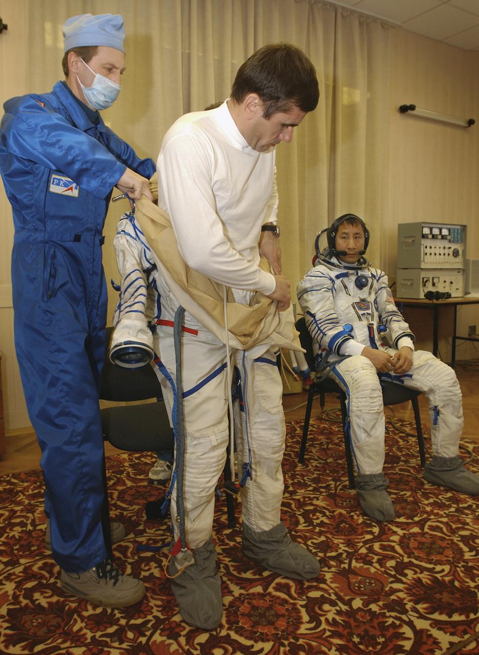Expedition 7 Commander Yuri I. Malenchenko, center, dons his Russian Sokol suit for the leak check, seat liner check and Soyuz inspection at the Soyuz Integration Facility at the Baikonur Cosmodrome in Baikonur, Kazakhstan, Thursday, April 10, 2003. Seated is astronaut Edward T. Lu, NASA International Space Station Science Officer and Flight Engineer for Expedition 7. Photo Credit: (NASA/Bill Ingalls)