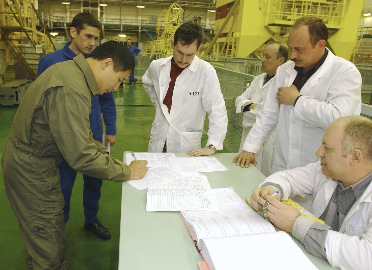 Astronaut Edward T. Lu, NASA International Space Station science officer and flight engineer for Expedition 7, left, signs documents after the suit leak check, seat liner check, and Soyuz inspection at the Baikonur Cosmodrome, Building 254, Soyuz Integration Facility in Kazakhstan, Thursday April 10, 2003. Cosmonaut Yuri I. Malenchenko, Expedition 7 commander, second left, watches as the documents are being signed. Photo Credit: (NASA/Bill Ingalls)