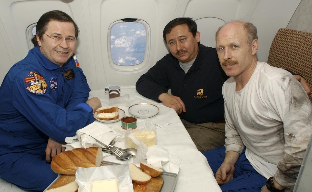 Expedition 6 Flight Engineer Nikolai Budarin, left, Cosmonaut Talgat Musabayev, and Commander Ken Bowersox, right, share a meal onboard the aircraft during their flight from Kazakhstan to Moscow on Tuesday, May 4, 2003.    Photo Credit: (NASA/Bill Ingalls)