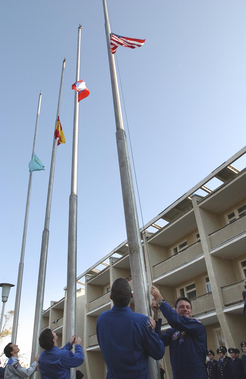 Expedition 8 Commander and NASA Science Officer Michael Foale, right, is joined by his backup, Bill McArthur outside the Cosmonaut Hotel Tuesday, Oct. 14, 2003, for the traditional raising of the flags of the crewmembers who will launch Saturday, Oct. 18 on the Soyuz TMA-3 vehicle to the International Space Station in Baikonur, Kazahstan. European Space Agency Astronaut Pedro Duque, far left, and Expedition 8 Soyuz Commander Alexander Kaleri who will launch with Foale, raise the flags of Spain and Russia outside their hotel. Photo Credit (NASA/Bill Ingalls)