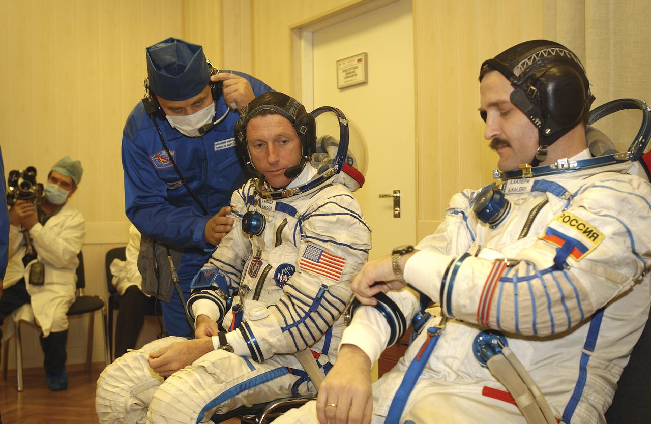 Expedition 8 Commander and NASA Science Officer Michael Foale, seated left, looks at Expedition 8 Soyuz Commander Alexander Kaleri as he makes an adjustment while suiting up, Saturday, Oct. 18, 2003, at the Baikonur Cosmodrome in Kazakhstan prior to their departure for the launch pad with European Space Agency astronaut Pedro Duque. The trio were launched on a Soyuz TMA-3 vehicle to the International Space Station, arriving on Oct. 20. Photo Credit (NASA/Bill Ingalls)