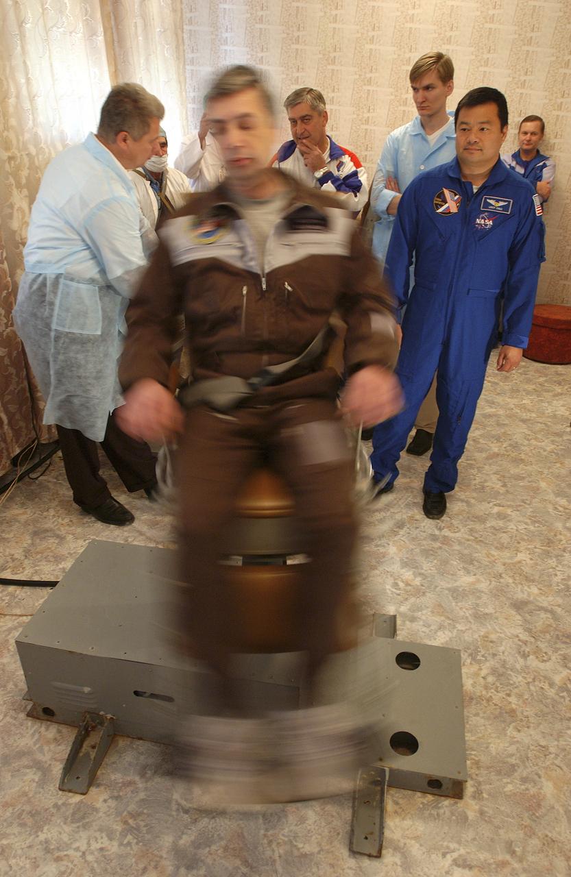 Expedition 10 Commander Leroy Chiao, right, looks on as Russian Space Forces cosmonaut Yuri Shargin takes a spin in a rotating chair at their crew quarters in Baikonur, Kazakhstan, Friday, October 8, 2004, as they prepare for launch to the International Space Station October 14 with Flight Engineer and Soyuz Commander Salizhan Sharipov. The chair is designed to condition the crewmembers' vestibular system against the effects of weightlessness once on orbit.  Photo Credit: (NASA/Bill Ingalls)