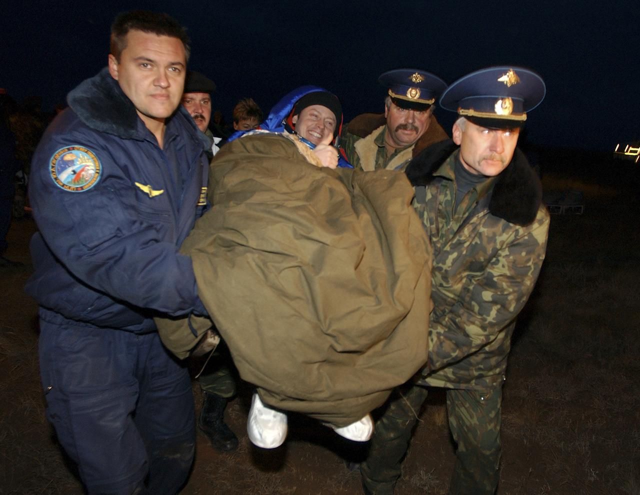 Expedition 9 Flight Engineer Michael Fincke is carried in a chair from the landing site to the medical tent in order to remove his sokol suit.  Fincke landed in the Soyuz capsule along with Expedition 9 Commander Gennady Padalka and Russian Space Forces cosmonaut Yuri Shargin.  The crew landed in their Soyuz capsule approximately 85 kilometers northeast of Arkalyk in northern Kazakhstan, Sunday, October 24, 2004.  Photo Credit: (NASA/Bill Ingalls)