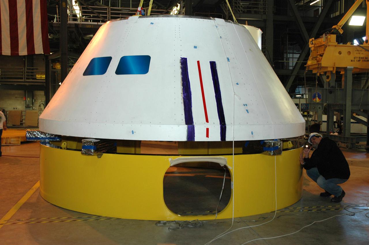 CAPE CANAVERAL, Fla. – – In high bay 4 of the Vehicle Assembly Building at NASA's Kennedy Space Center in Florida, a worker examines the Ares I-X crew module simulator as it is lowered onto a stand.  Ares I-X is the test flight for the Ares I.  The I-X flight will provide NASA an early opportunity to test and prove hardware, facilities and ground operations associated with Ares I. The launch of the 327-foot-tall, full-scale Ares I-X, targeted for July 2009, will be the first in a series of unpiloted rocket launches from Kennedy. When fully developed, the 16-foot diameter crew module will furnish living space and reentry protection for the astronauts.  Photo credit: NASA_Tim Jacobs