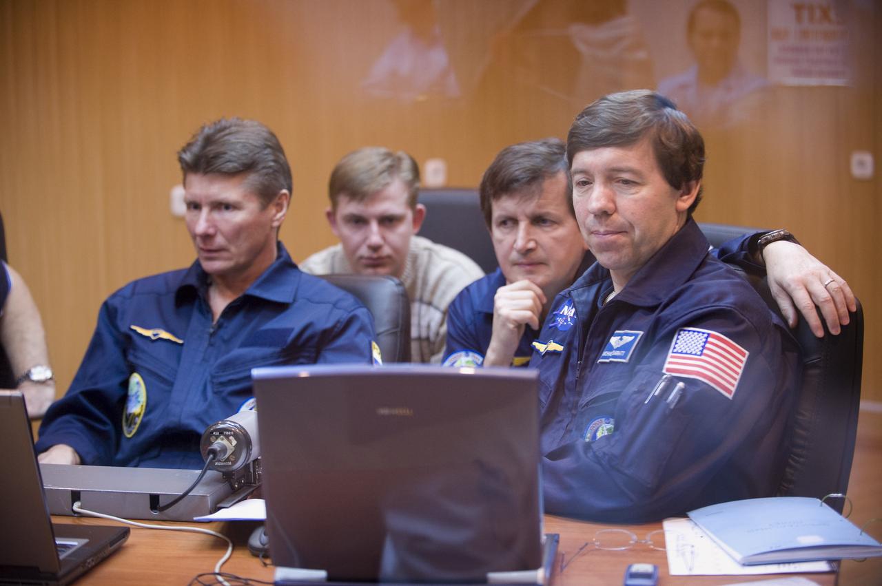 Expedition 19 Commander Gennady I. Padalka, left, Flight Engineer Michael R. Barratt, right, and Spaceflight Participant Charles Simonyi, 2nd row right, along with cosmonaut instructors are seen through a quarantine windowed room as they participate in Soyuz rendezvous and docking training at the Cosmonaut Hotel, Saturday, March 21, 2009 in Baikonur, Kazakhstan.  (Photo Credit: NASA/Bill Ingalls)