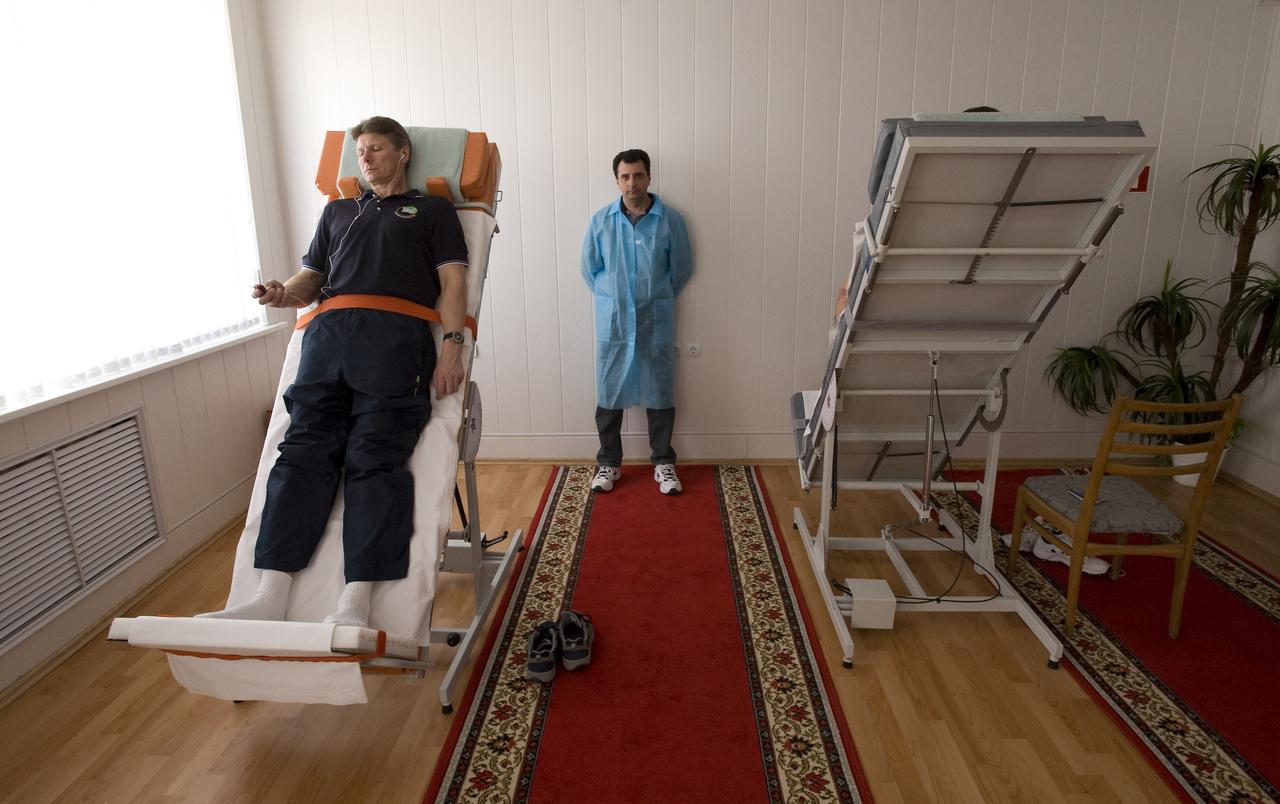 Expedition 19 Commander Gennady I. Padalka, left, listens to his mp3 player as a medical doctor looks on during the he participates tilt table training at the Cosmonaut Hotel, Saturday, March 21, 2009 in Baikonur, Kazakhstan. Expedition 19 Flight Engineer Michael R. Barratt in on the tilt table on the right. (Photo Credit: NASA/Bill Ingalls)