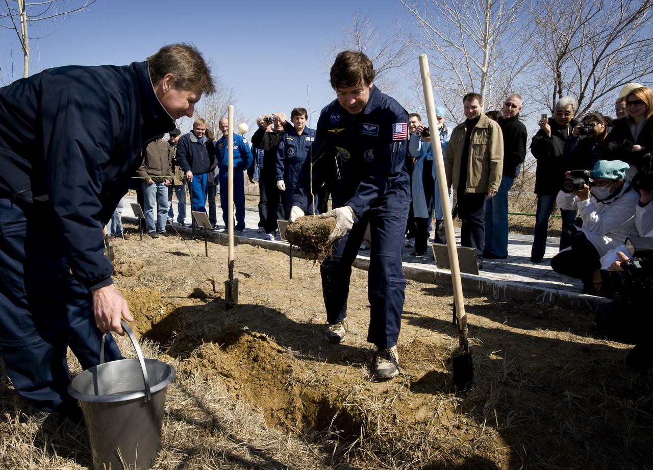 Expedition 19 Commander Gennady I. Padalka, left, watches as Flight Engineer Michael R. Barratt plants a tree during the traditional tree planting ceremony at the Cosmonaut Hotel, Saturday, March 21, 2009 in Baikonur, Kazakhstan.  (Photo Credit: NASA/Bill Ingalls)