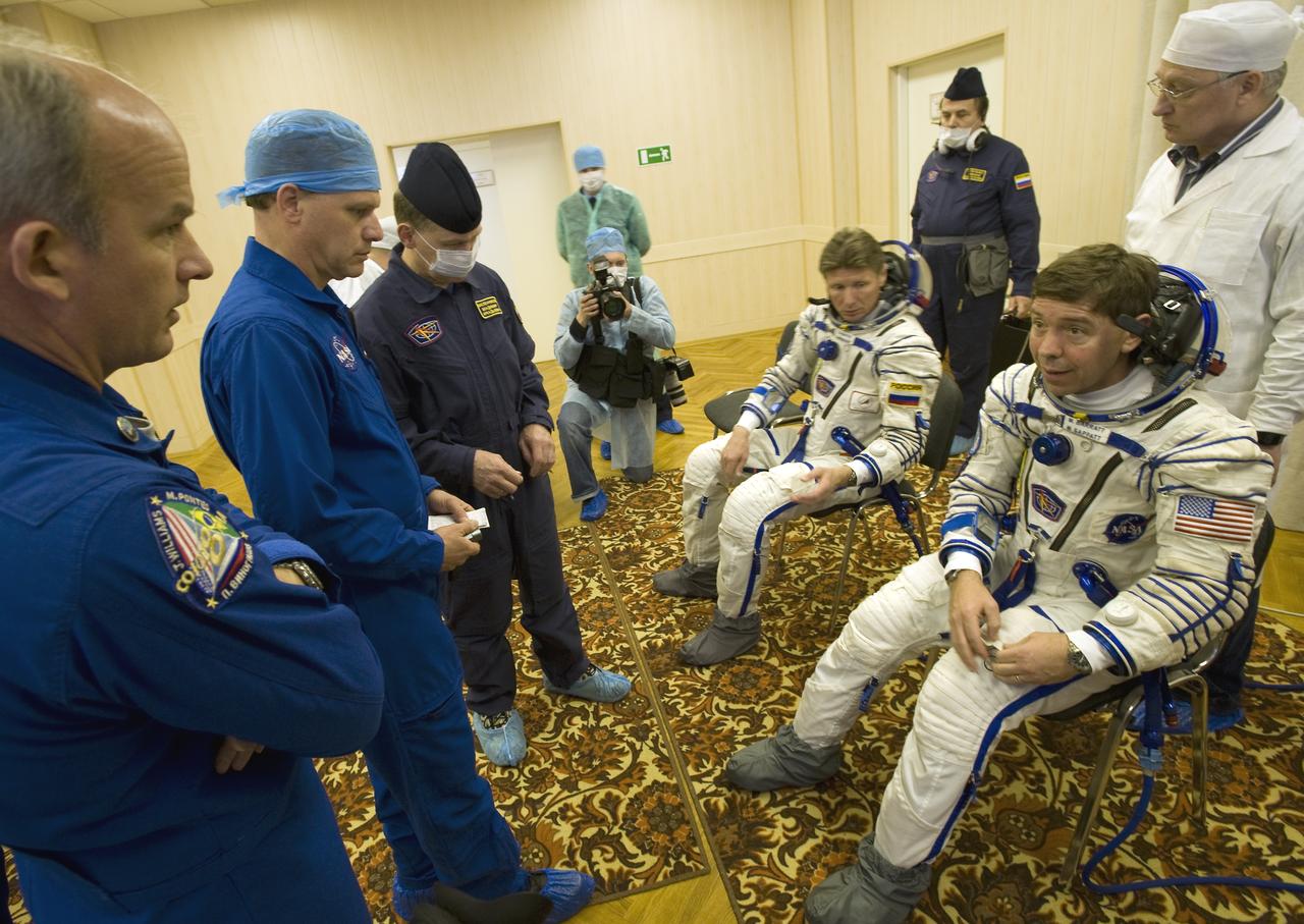 Expedition 19 backup commander Jeffrey Williams, left, NASA Flight Surgeon Ed Powers, M.D., 2nd from left, talk with Expedition 19 Flight Engineer Michael R. Barratt, far right, as he and fellow crew member Expedition 19 Commander Gennady I. Padalka don their Sokol flights suits in preparation for their Soyuz launch to the International Space Station with Spaceflight Participant Charles Simonyi on Thursday, March 26, 2009 in Baikonur, Kazakhstan. (Photo Credit: NASA/Bill Ingalls)