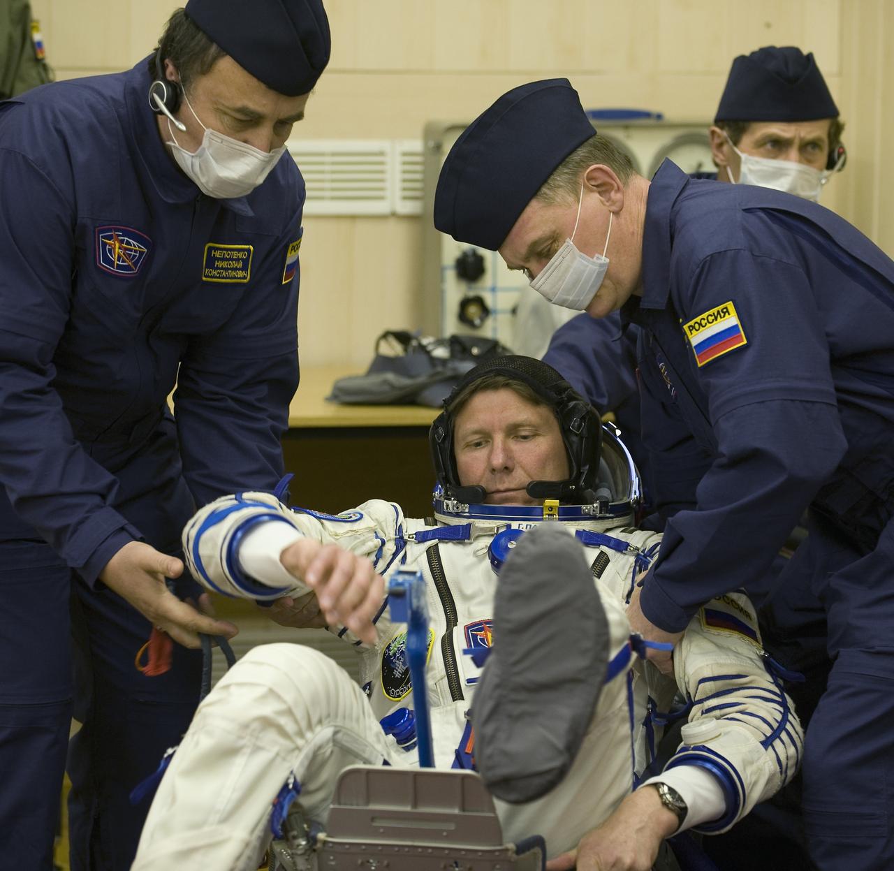 Expedition 19 Commander Gennady I. Padalka is helped into a seat where his suit will be pressure checked in preparation for his Soyuz launch to the International Space Station with Flight Engineer Michael R. Barratt and Spaceflight Participant Charles Simonyi on Thursday, March 26, 2009 in Baikonur, Kazakhstan. (Photo Credit: NASA/Bill Ingalls)