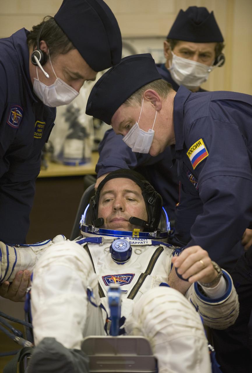 Expedition 19 Flight Engineer Michael R. Barratt is helped into a seat where his suit will be pressure checked in preparation for his Soyuz launch to the International Space Station with Commander Gennady I. Padalka and Spaceflight Participant Charles Simonyi on Thursday, March 26, 2009 in Baikonur, Kazakhstan. (Photo Credit: NASA/Bill Ingalls)
