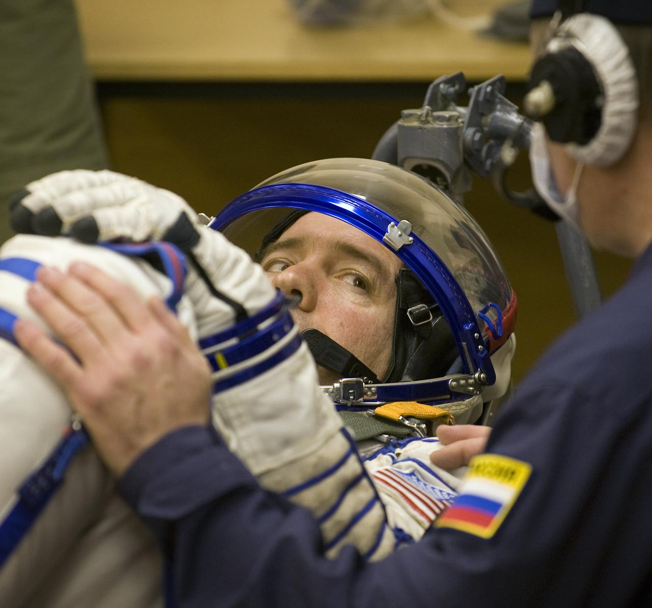 Expedition 19 Flight Engineer Michael R. Barratt listens to instructions prior to having his Russian Sokol suit pressure checked in preparation for his Soyuz launch to the International Space Station with Commander Gennady I. Padalka and Spaceflight Participant Charles Simonyi on Thursday, March 26, 2009 in Baikonur, Kazakhstan. (Photo Credit: NASA/Bill Ingalls)