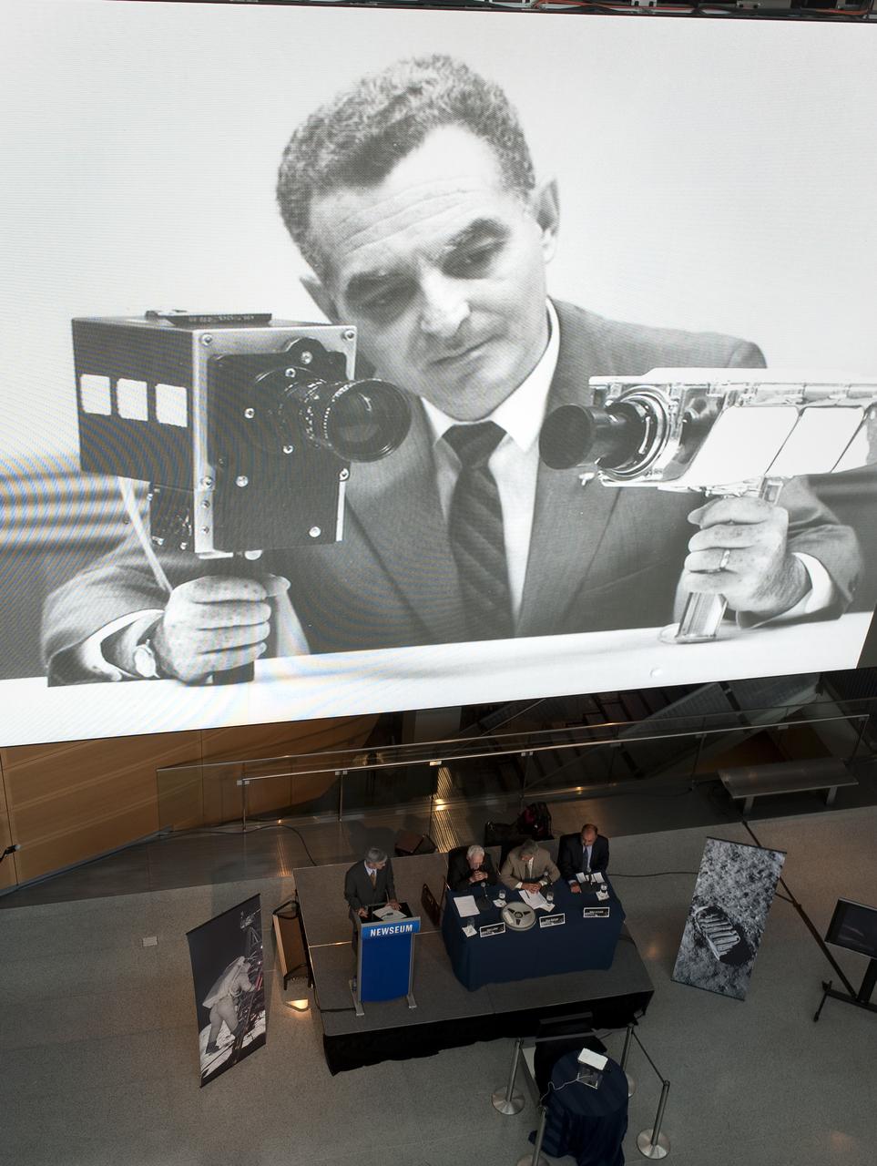 A photograph from the 1960's showing Stan Lebar, former Westinghouse Electric program manager, holding two cameras used during the Apollo missions is seen on a large video monitor above panelists, including Stan Lebar, at NASA's briefing where restored Apollo 11 moonwalk footage was revealed for the first time at the Newseum, Thursday, July 16, 2009, in Washington, DC.  Photo Credit: (NASA/Carla Cioffi)