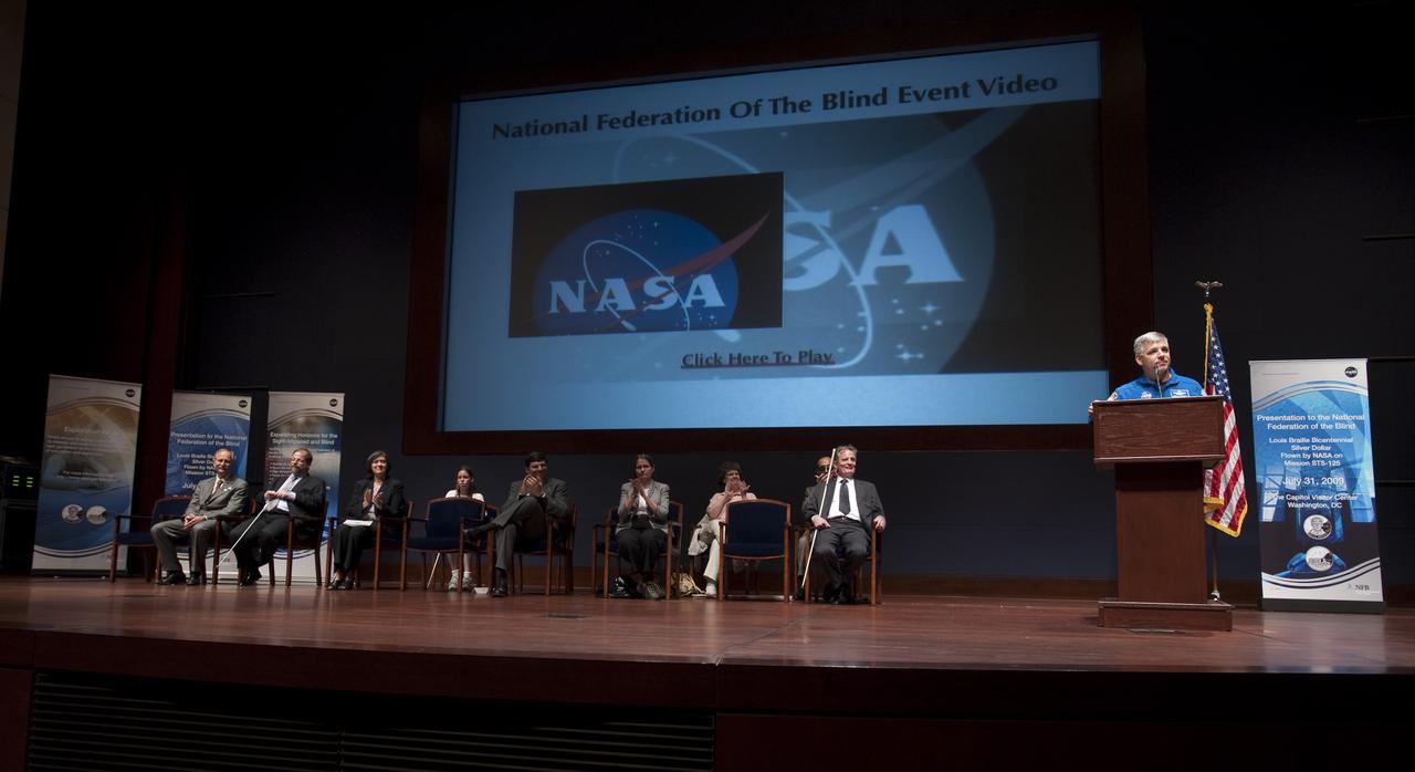 NASA astronaut Greg Johnson, at podium, speaks at a ceremony where senior NASA officials presented the National Federation of the Blind with two Louis Braille Bicentennial Silver Dollars that flew on Space Shuttle Atlantis' mission (STS-125) to the Hubble Space Telescope in May 2009, Friday evening, July 31, 2009, at the Capitol Visitors Center in Washington. Photo Credit: (NASA/Paul E. Alers)